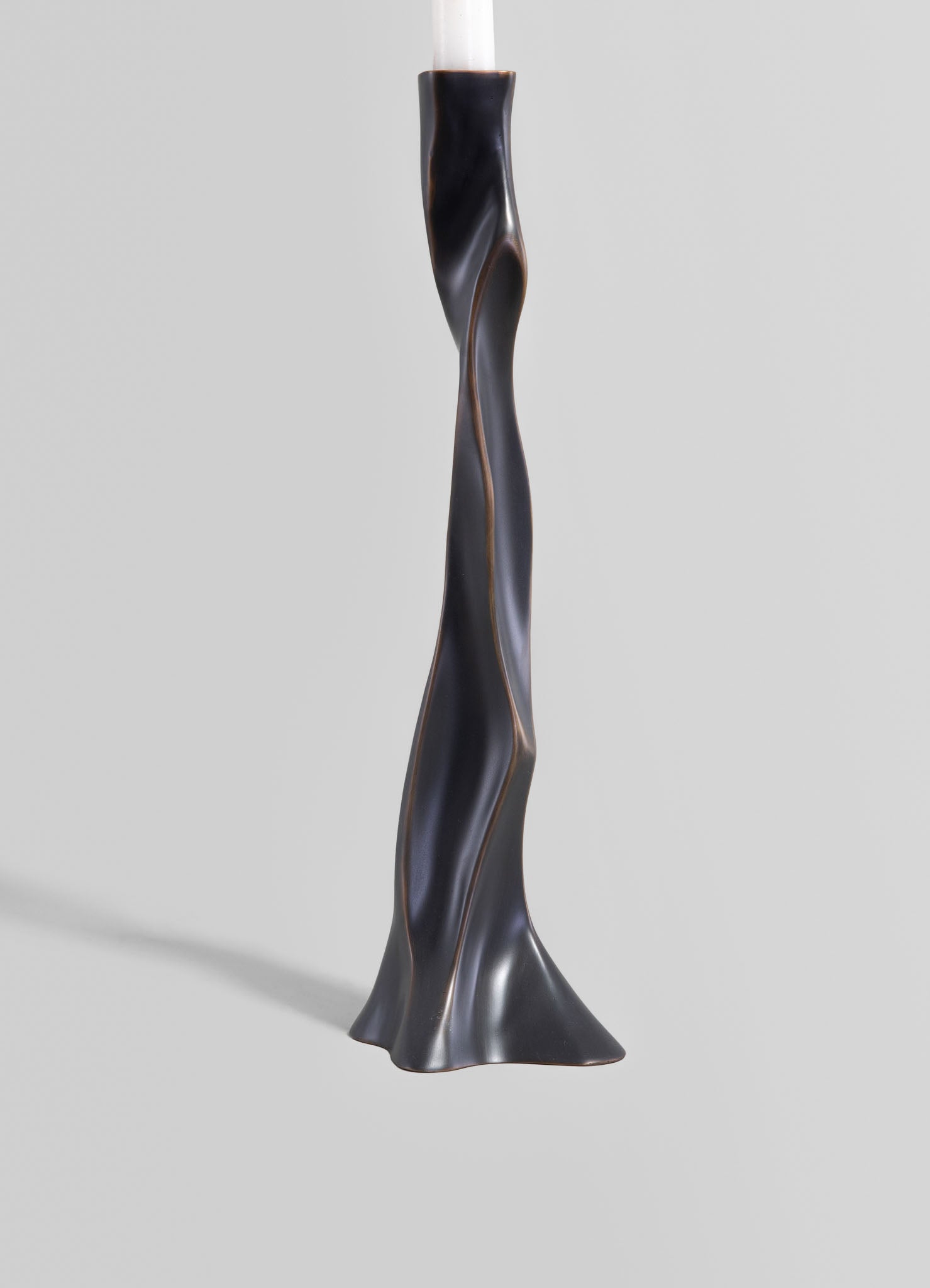 A sculptural candlestick holder made of black ceramic with a twisted, organic shape and a matte finish, designed to hold a taper candle.