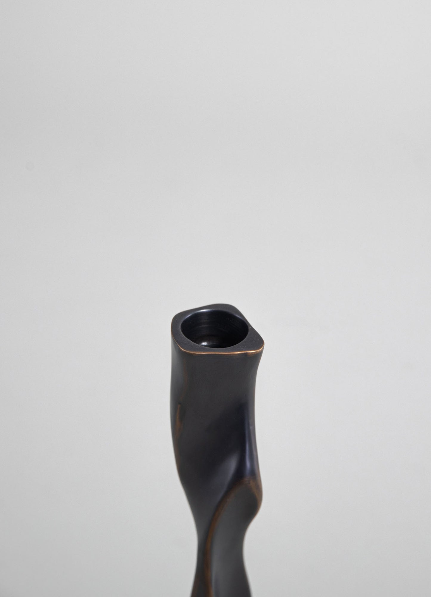 A black ceramic vase with a matte finish, featuring an organic, curved shape and a narrow opening at the top.