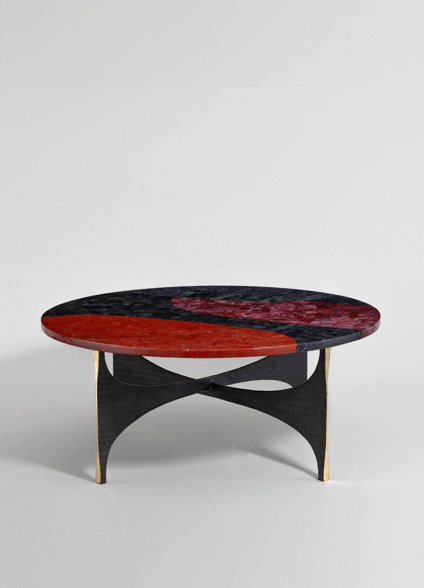 A coffee table with a circular top made of multicolored marble in red, black, and pink tones, featuring a curved black wood base with gold accents.