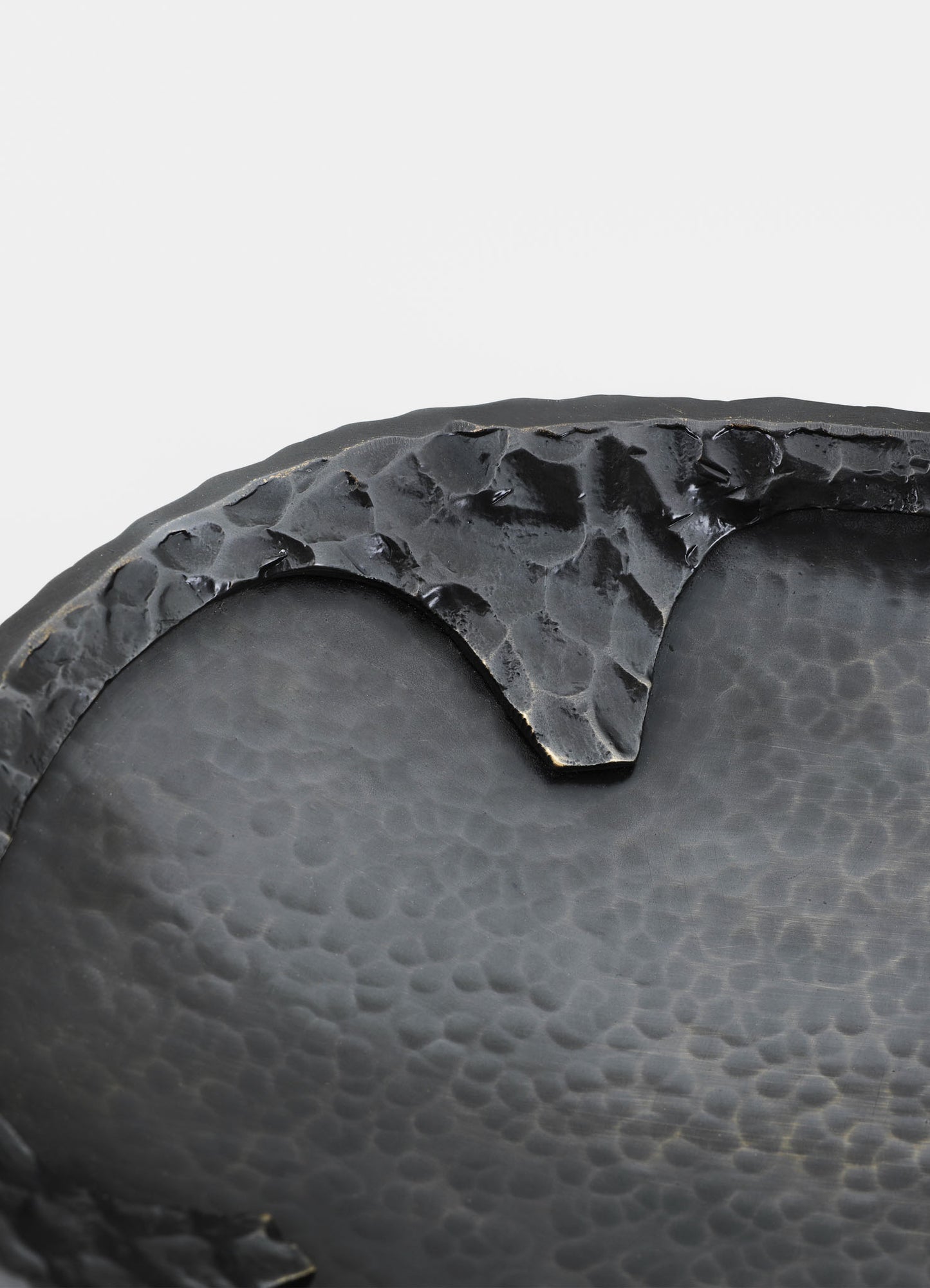 Close-up of a black ceramic bowl with a textured, hammered surface and a rough, uneven rim. The bowl features a matte finish and an organic, handcrafted aesthetic.