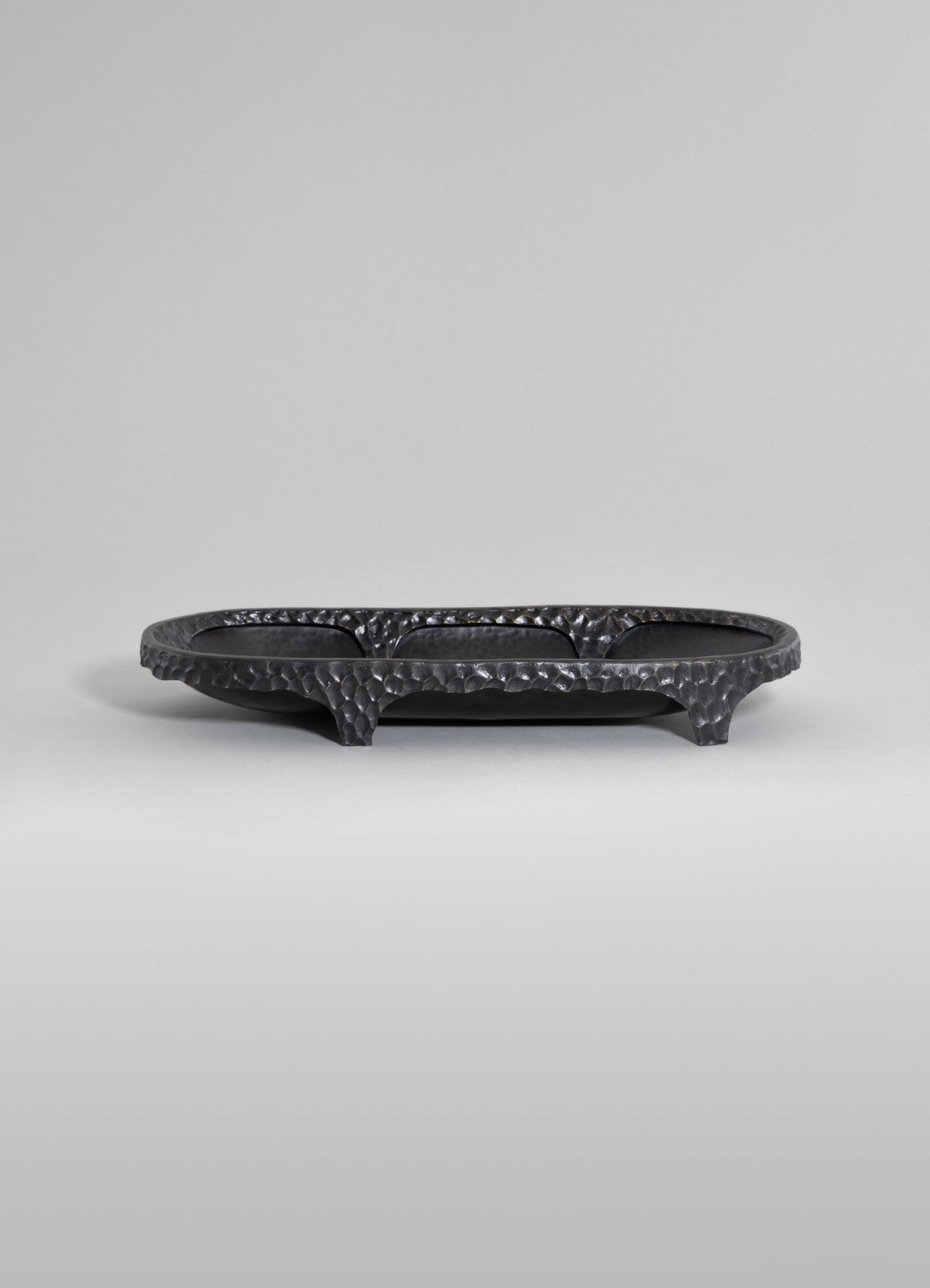 A black, hammered metal serving tray with a textured surface, raised edges, and short curved legs for stability.