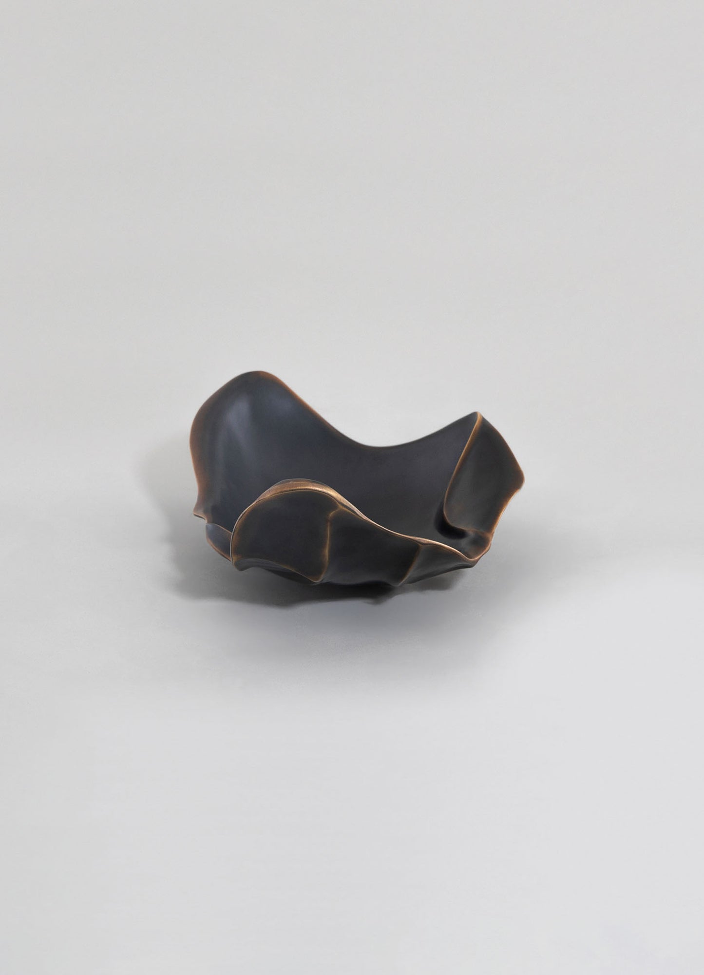 A decorative ceramic bowl with a matte black finish and wavy, organic edges, accented with subtle metallic gold detailing along the rim.