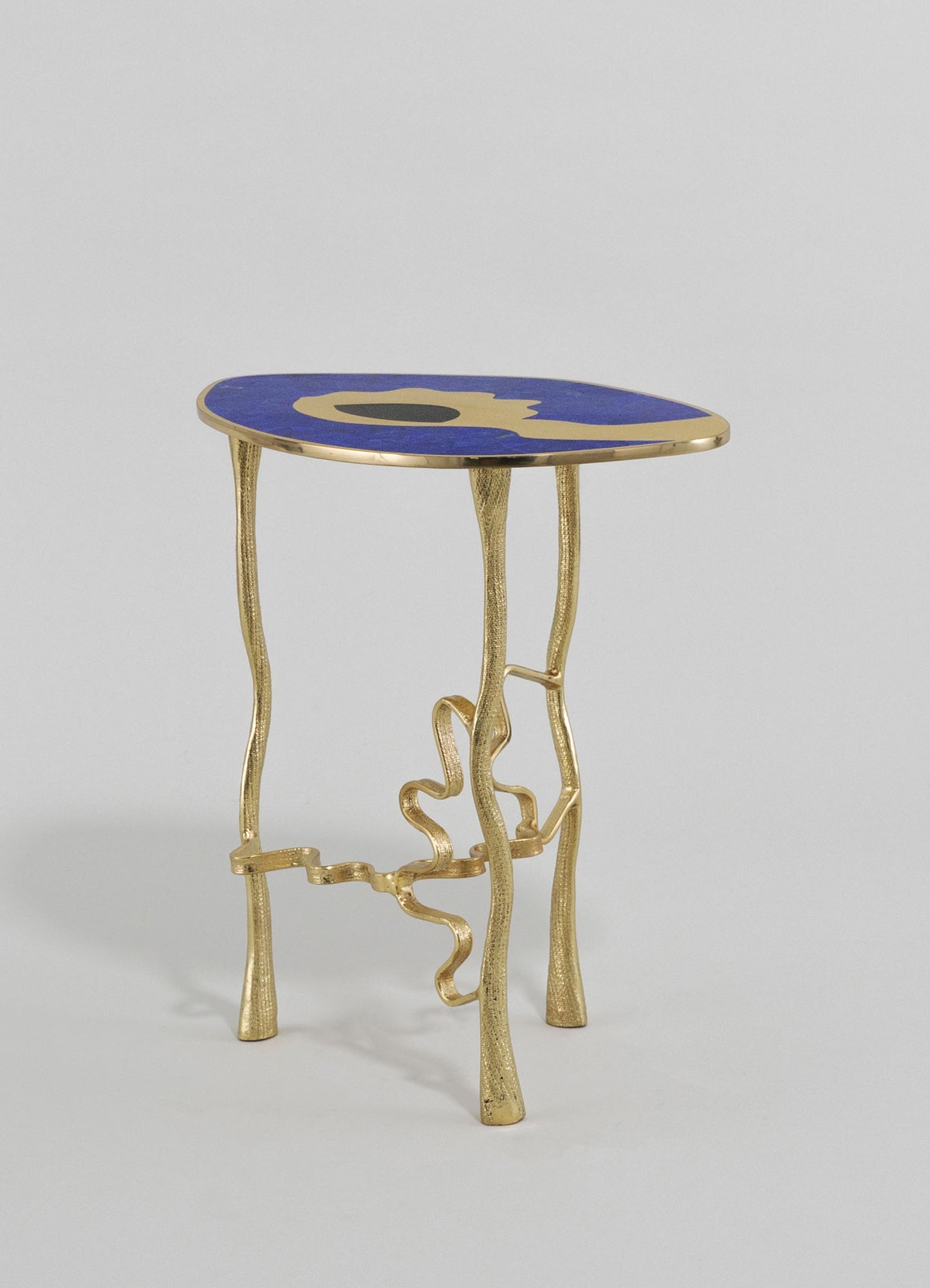 A side table with a rounded top featuring a blue surface with abstract gold and black motifs, supported by irregularly shaped, textured gold metal legs.