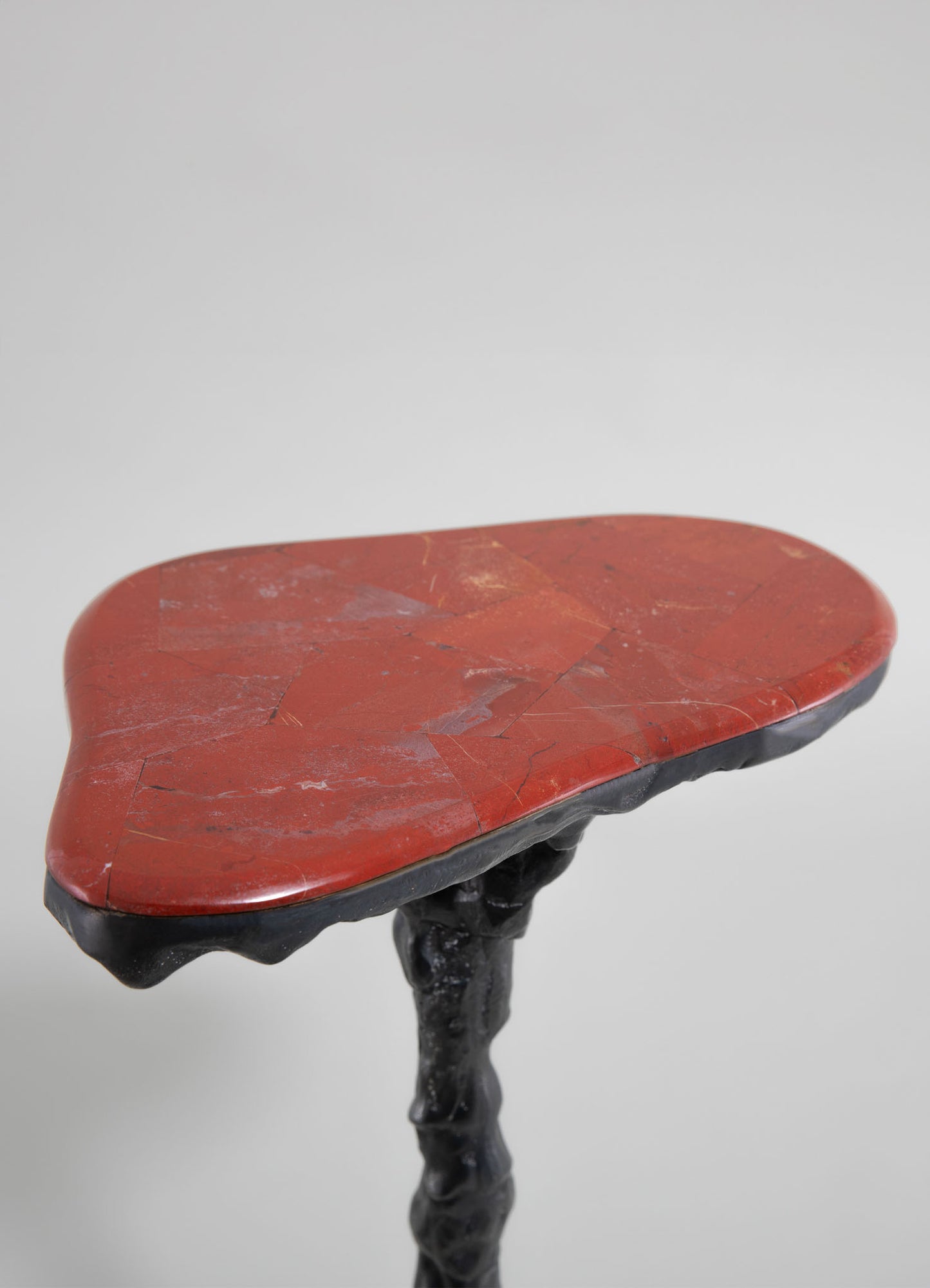 A small side table with a polished red stone top featuring natural cracks and variations, supported by a black carved wooden base with organic, twisting lines.