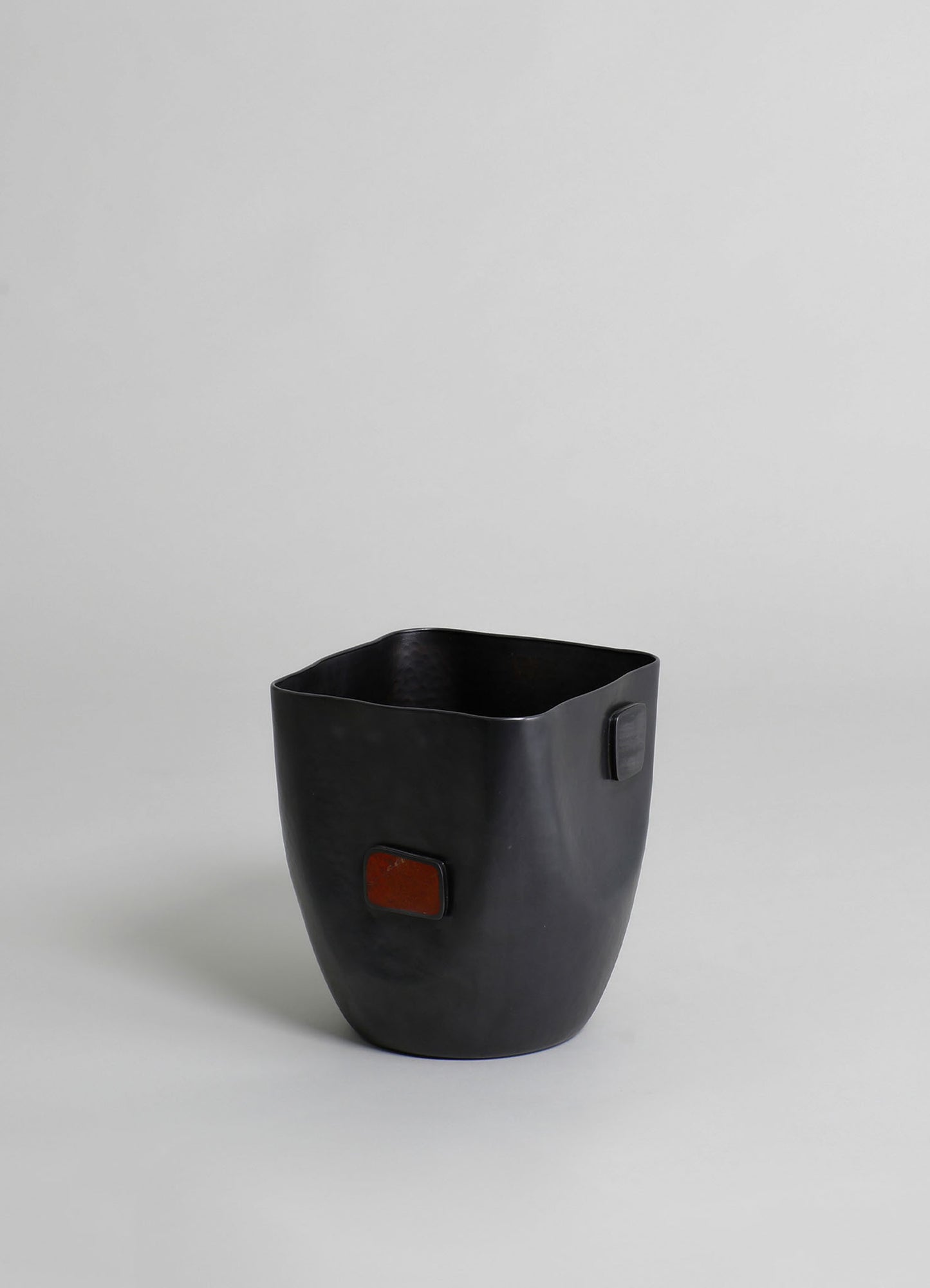 Black ceramic vase with a matte finish featuring rectangular accent details in dark red and gray, set against a plain light background.