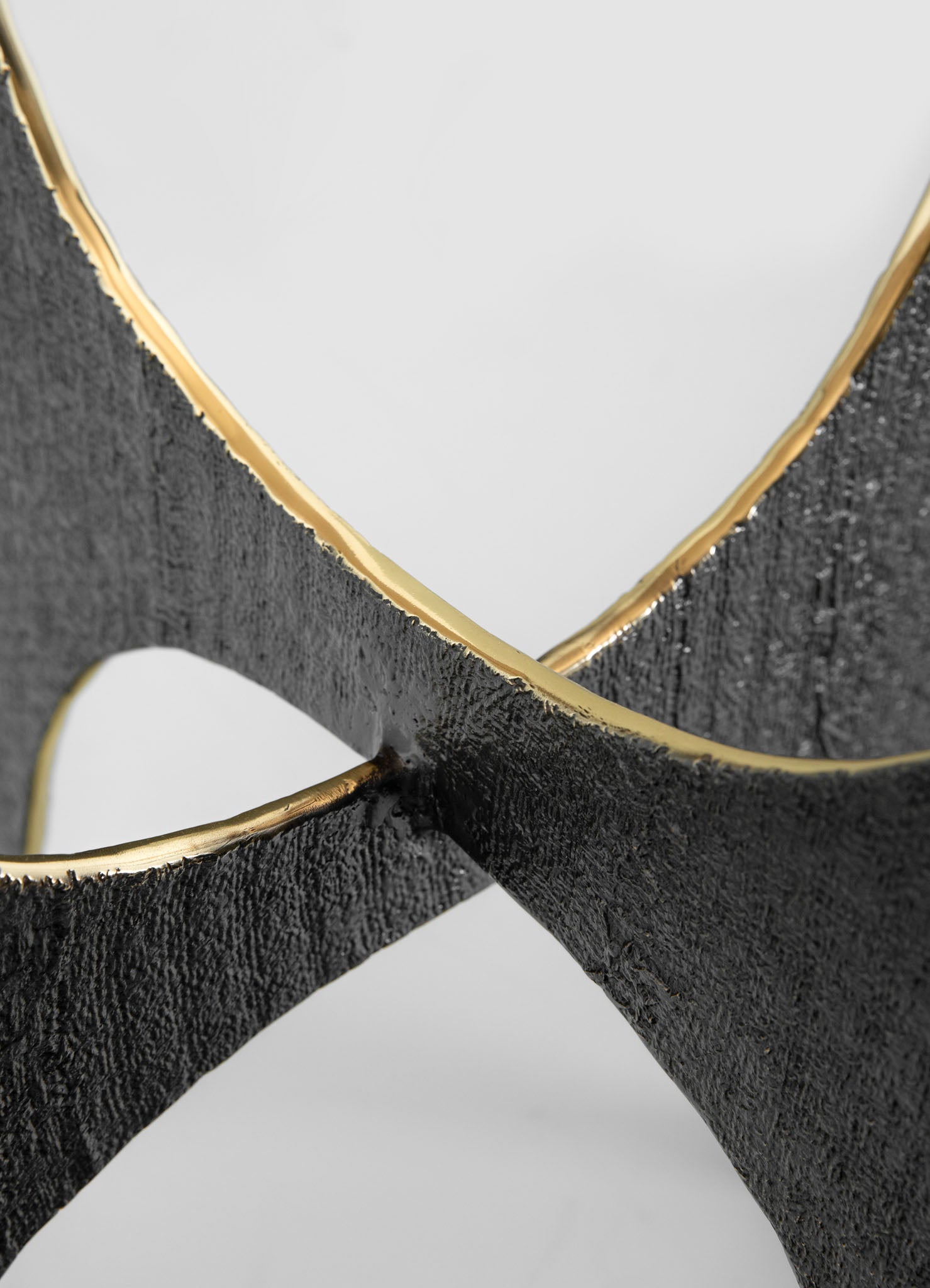 A close-up of a decorative object featuring intersecting black textured surfaces with smooth gold edges, forming an abstract geometric design. The materials appear to include textured black metal or stone and polished gold metal accents.