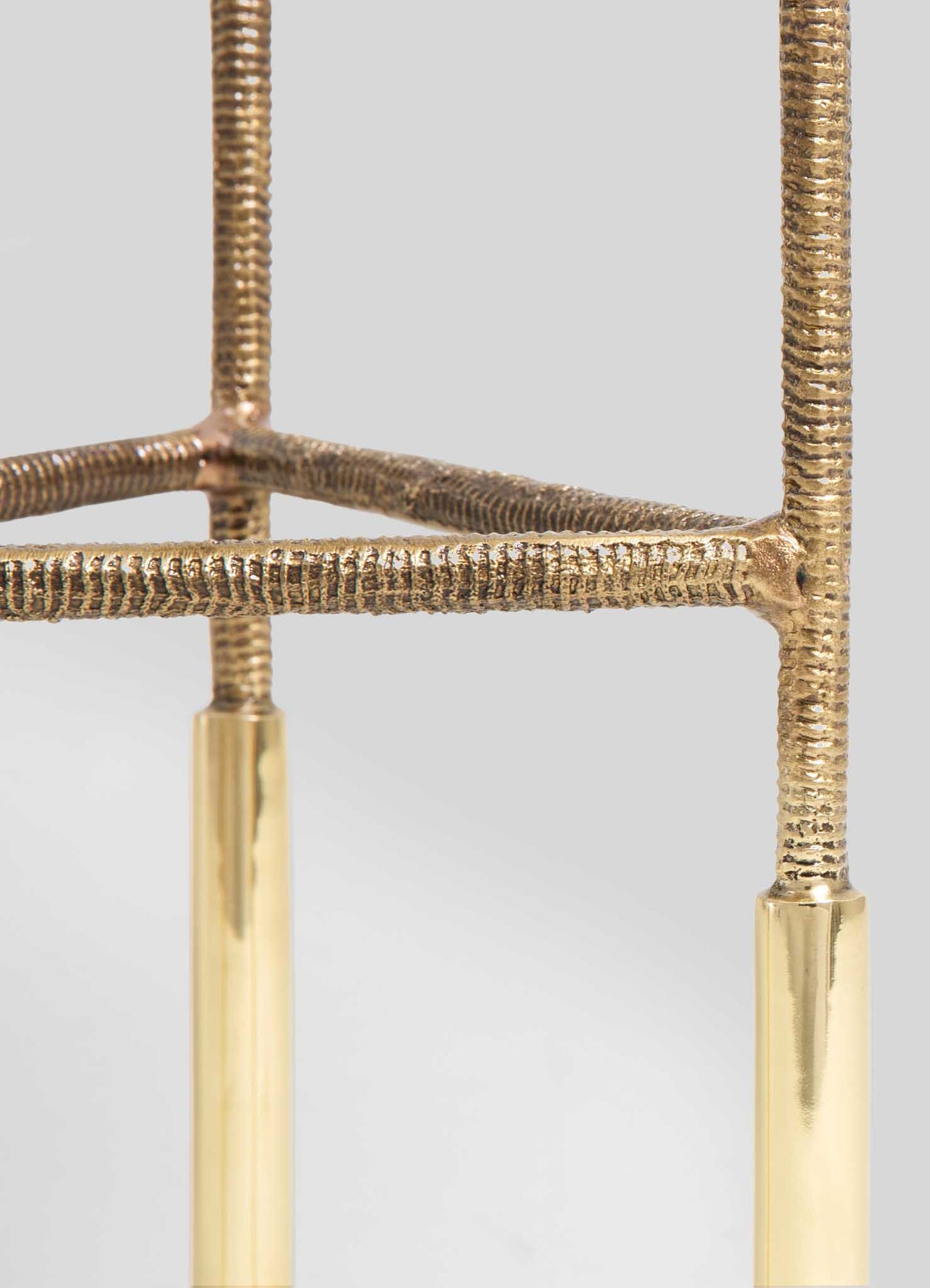 Close-up of a brass furniture leg with a textured, hammered finish, combined with smooth polished brass accents, on a light gray background.
