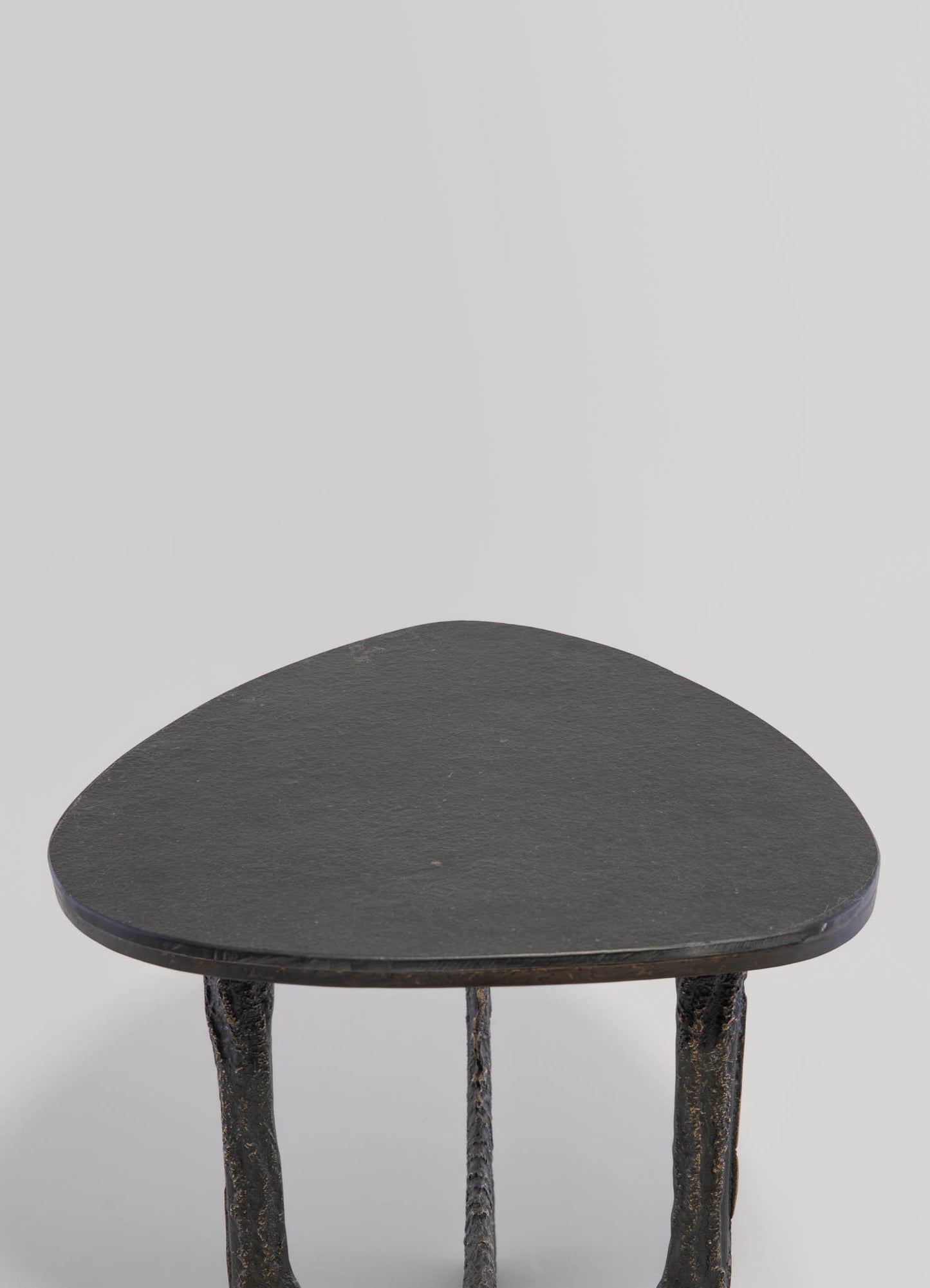 A small side table with a triangular black slate top and textured, irregular metal legs in a rustic, handcrafted style.