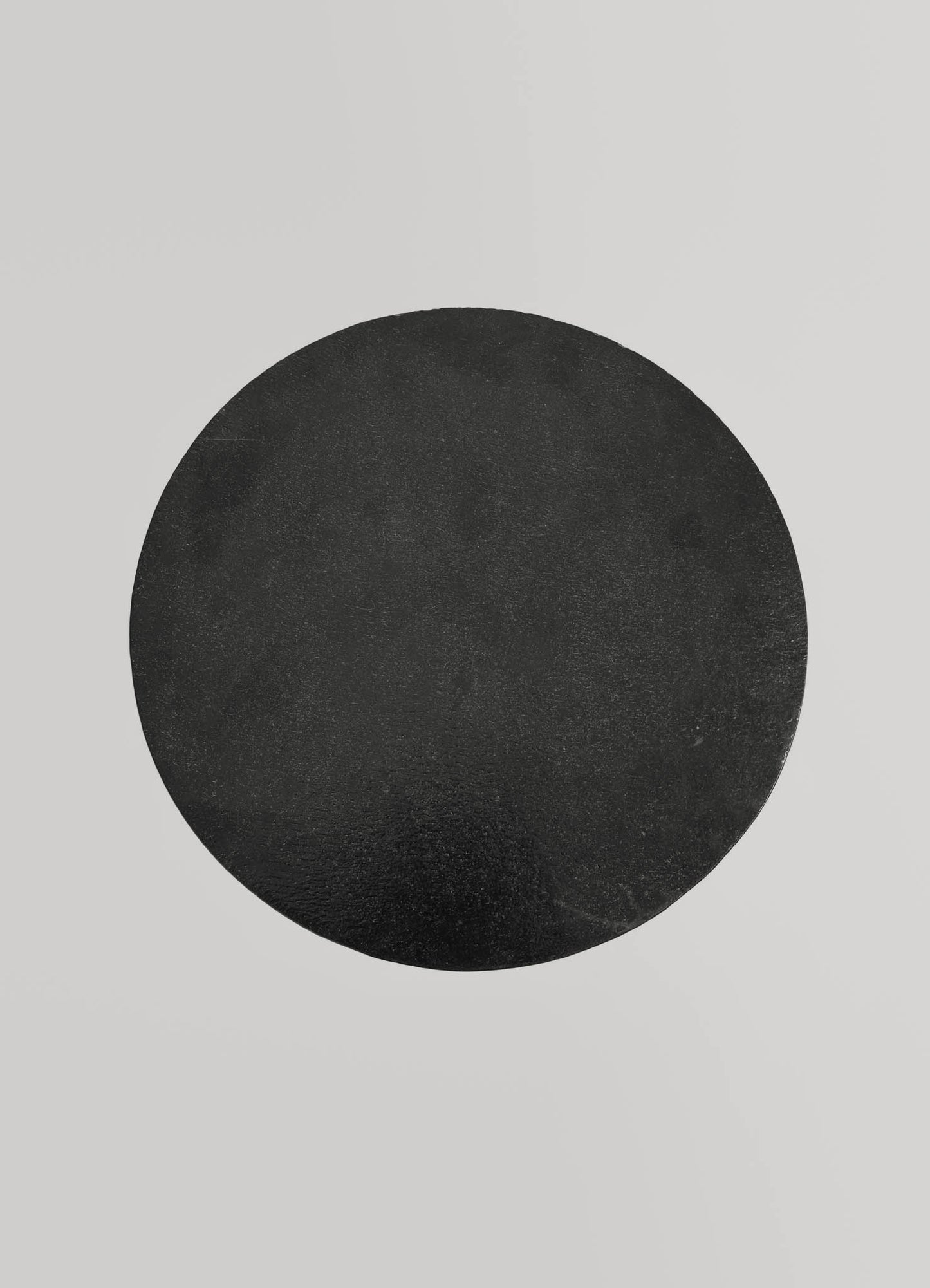 A black round stone or ceramic coaster with a matte finish, set against a light gray background.