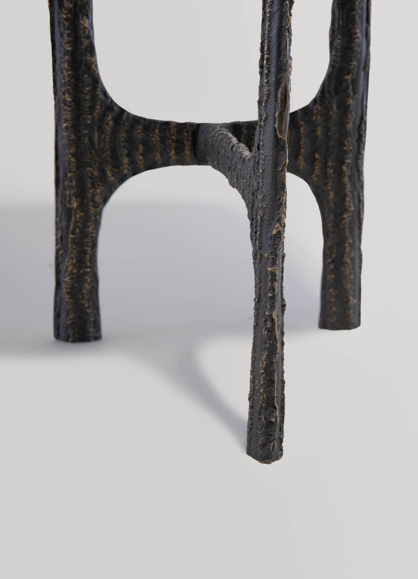Close-up of a black cast iron table leg with a textured, rough surface and an industrial style. The leg features a curved, rounded design with a matte finish, set against a plain, light background.