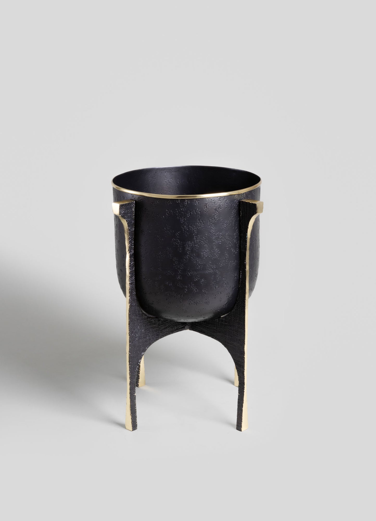 A black cast iron planter with a textured surface, supported by a black and gold-finished metal stand with curved legs.