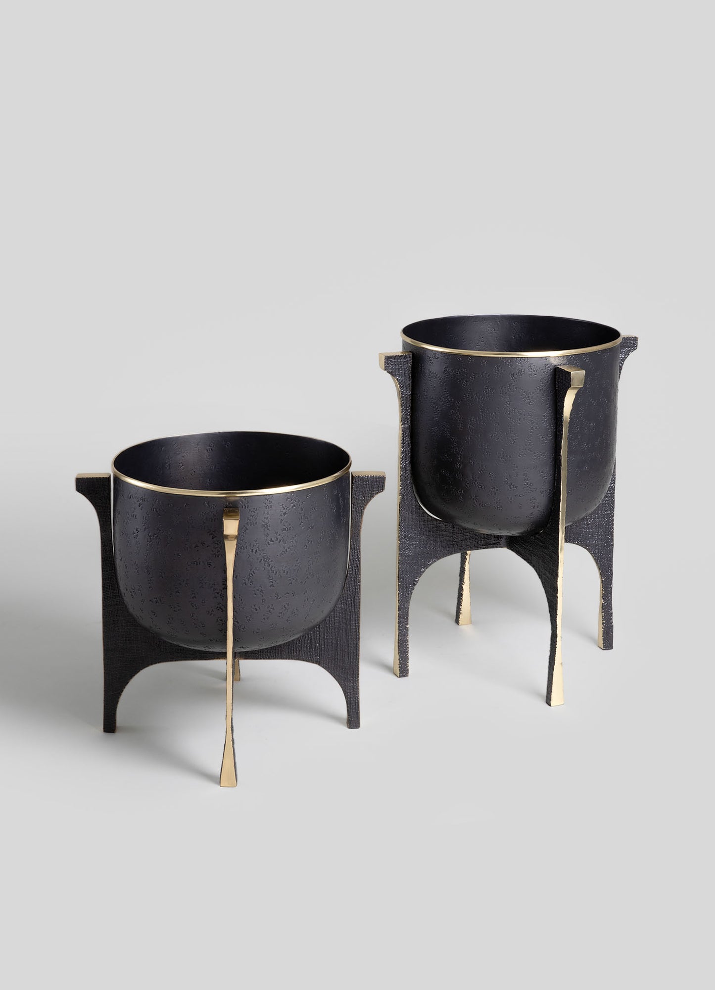 Pair of black textured metal bowls with gold accents on stand bases, featuring a contemporary design and sleek, curved shapes.