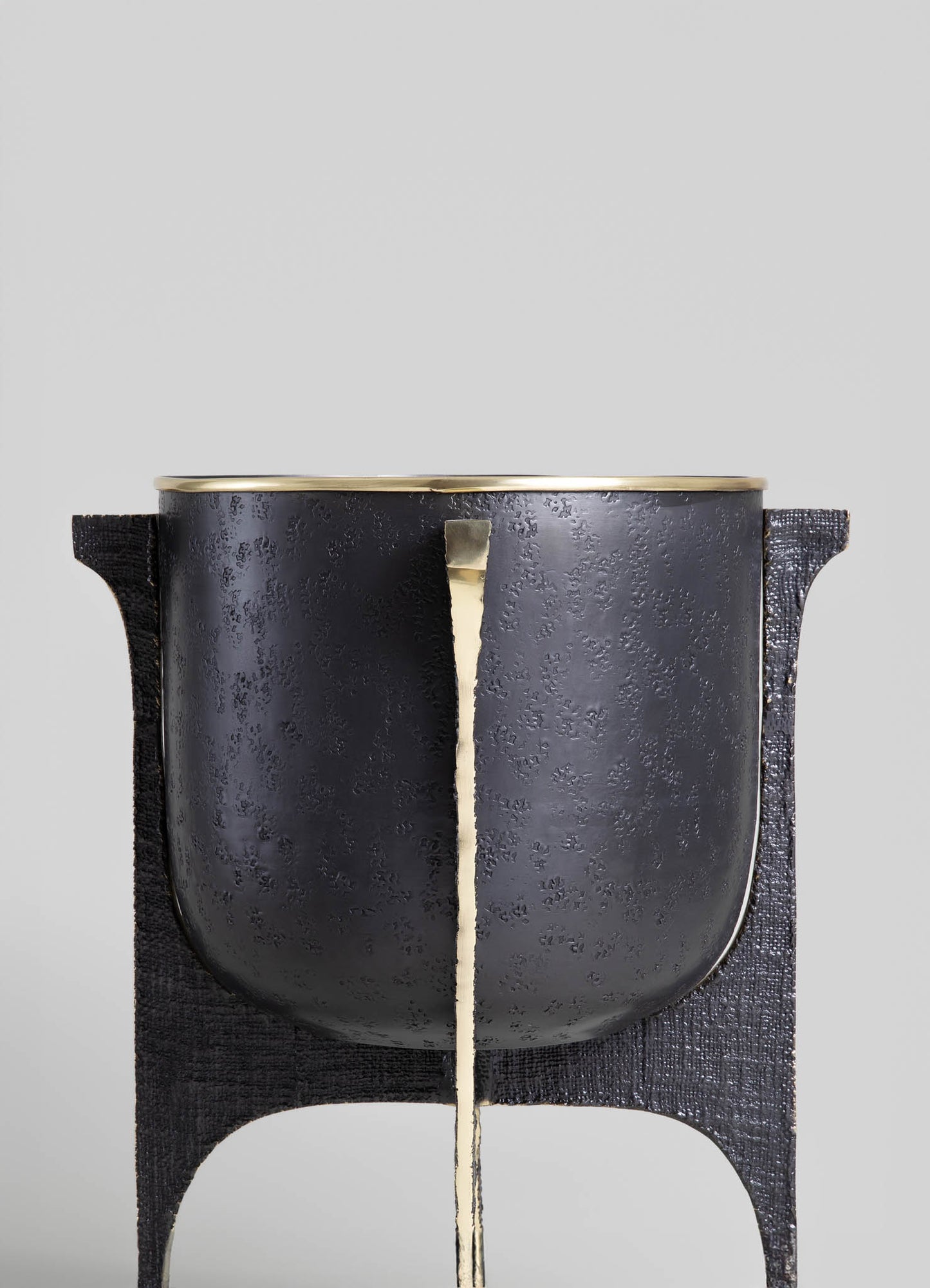 A black textured metal planter with a gold lining on the rim, mounted on a black wooden stand with curved cutouts. The overall style is modern with a minimalist design.