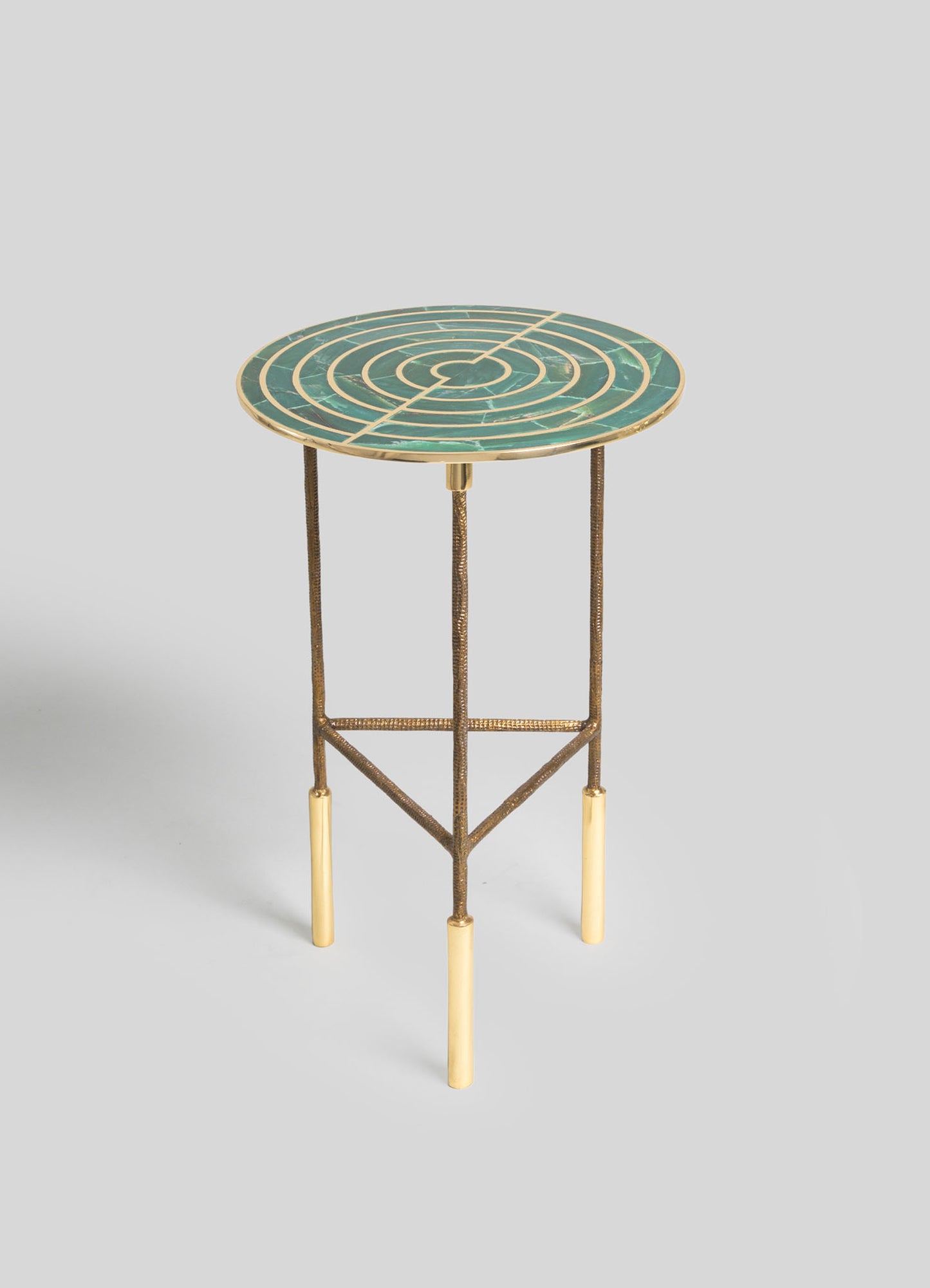 A round side table with a mosaic marble top featuring concentric circular patterns in shades of green, with metallic gold edging. The table has a metal frame with a textured, antique gold finish and four slim legs with gold accents.