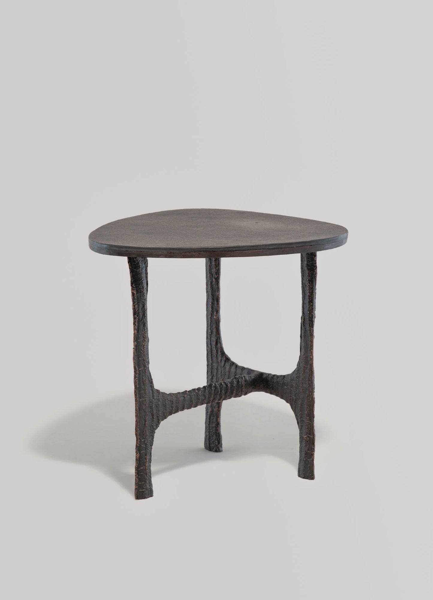A side table with a dark wooden top featuring an asymmetrical, leaf-like shape, supported by textured, branch-like legs made of carved wood with a natural, rustic finish.