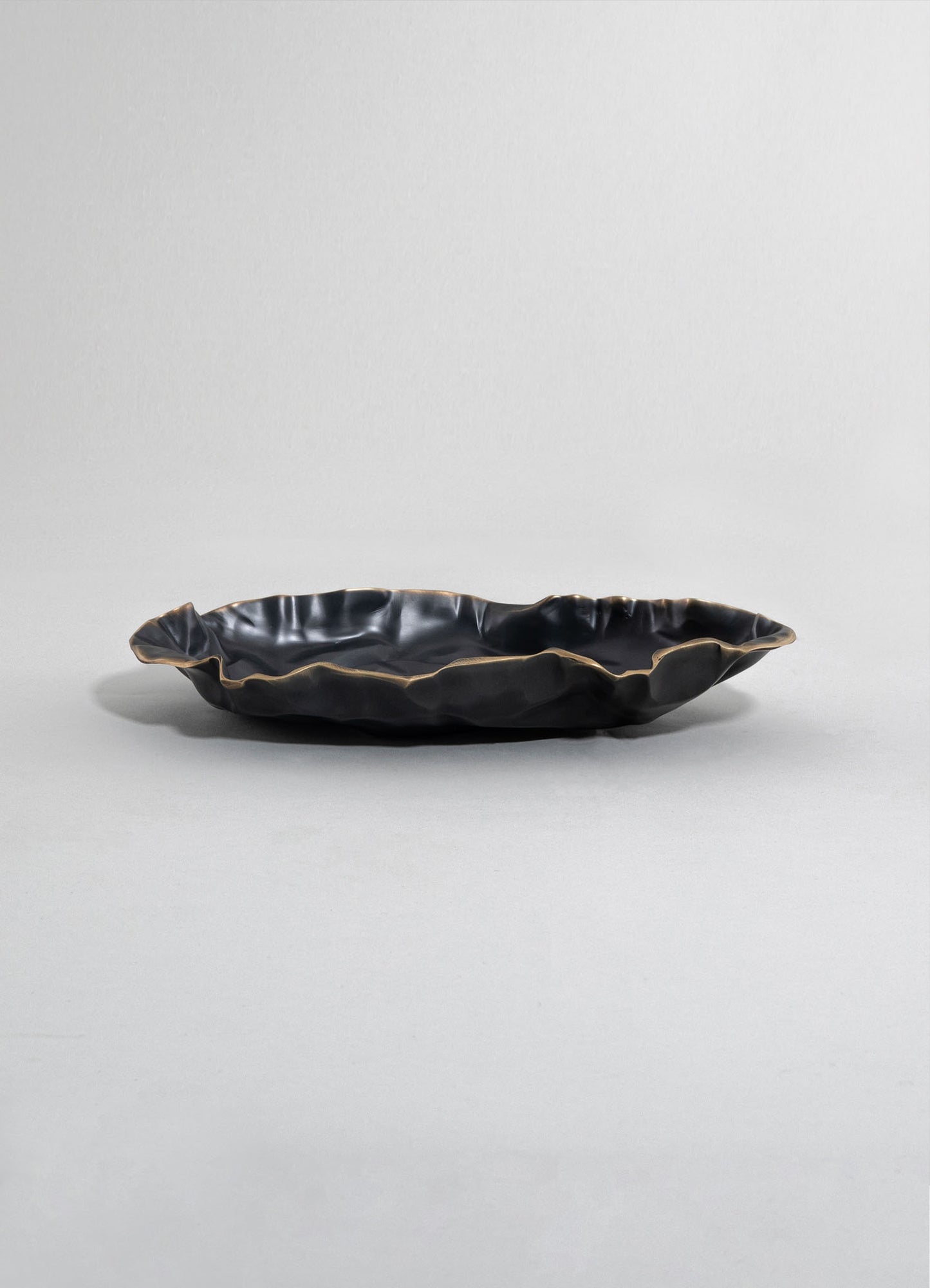 A black ceramic tray with a wavy, irregular edge and a matte finish, designed with a contemporary and handcrafted style.