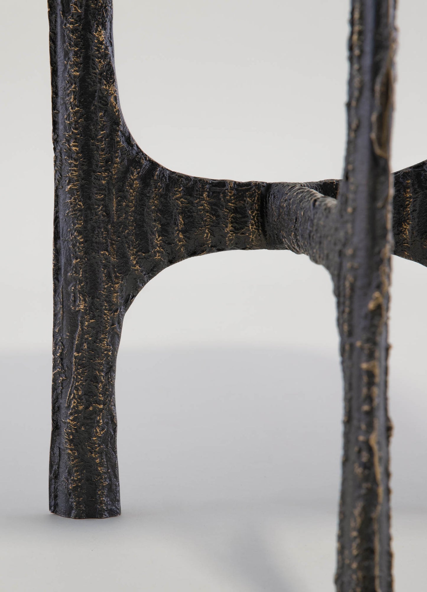 Close-up of a black, textured metal chair leg with a rough, hammered finish and curved design, set against a plain background.