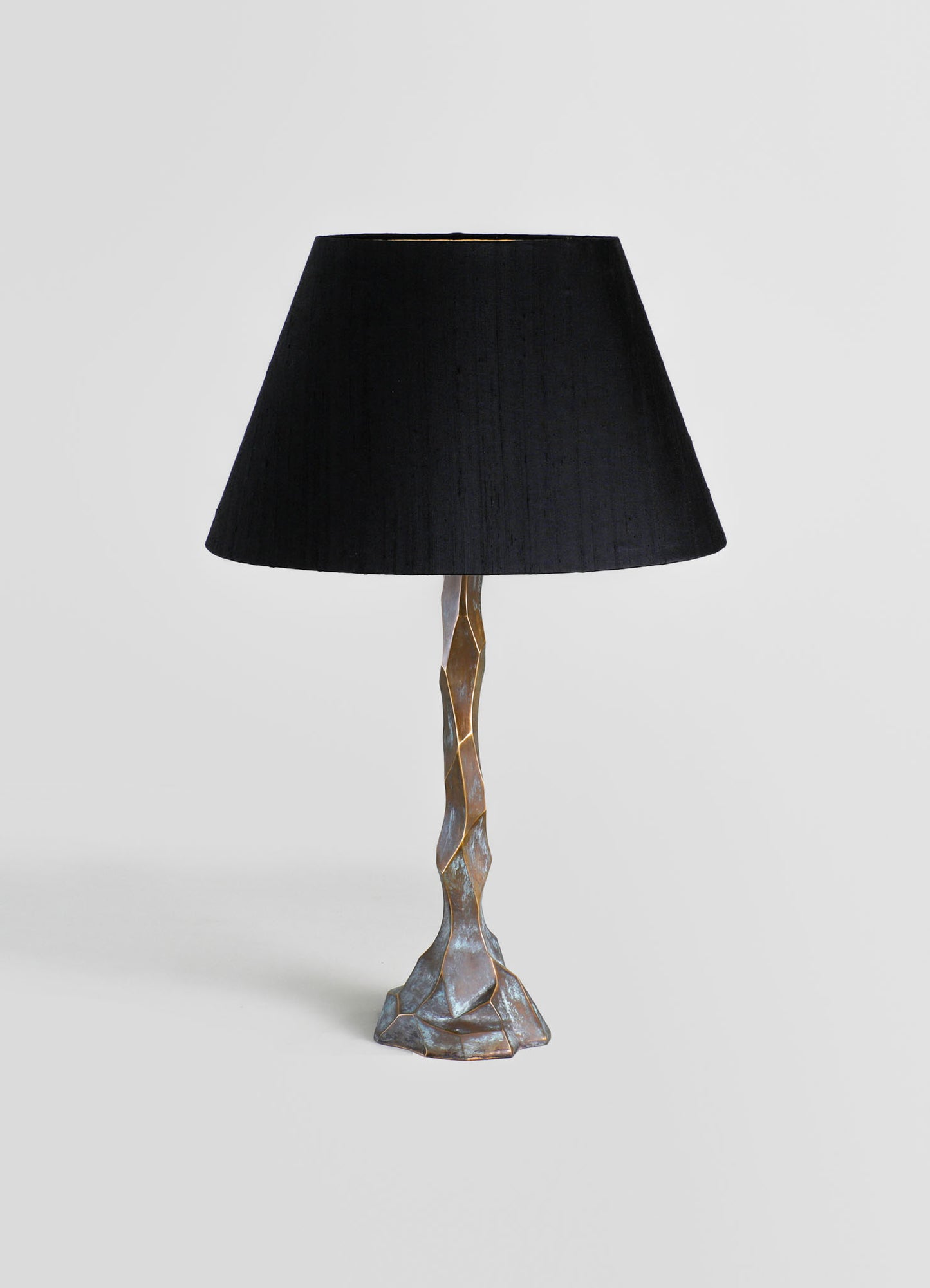 Table lamp with a textured, irregular metal base in a bronze finish and a broad black fabric lampshade, exhibiting a contemporary and artisanal style.