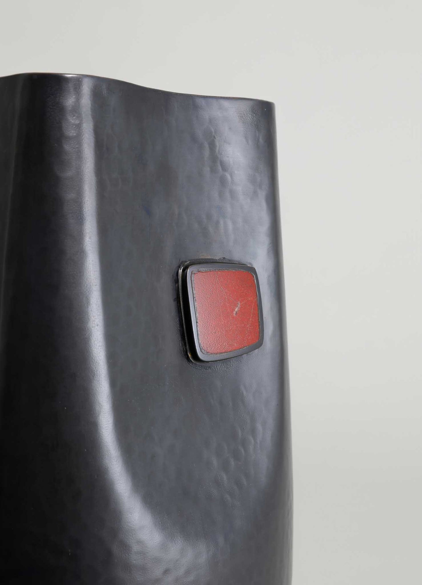 A black cylindrical object made of textured metal with a matte finish, featuring a rectangular red switch or button on its surface.