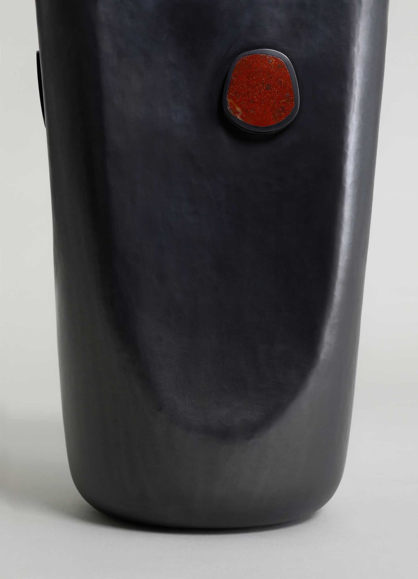A tall, cylindrical black vase with a smooth matte finish and an oval-shaped reddish-brown accent detail on the surface.