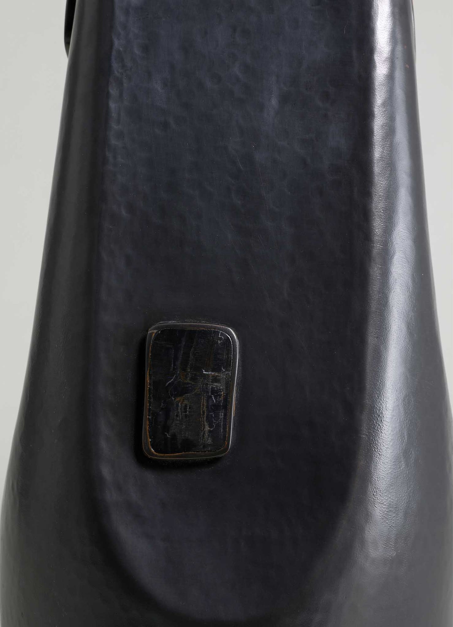 A black leather item with a textured surface and a small rectangular metal or plastic attachment. The style appears contemporary with a minimalist design, possibly a piece of luggage or a accessory.
