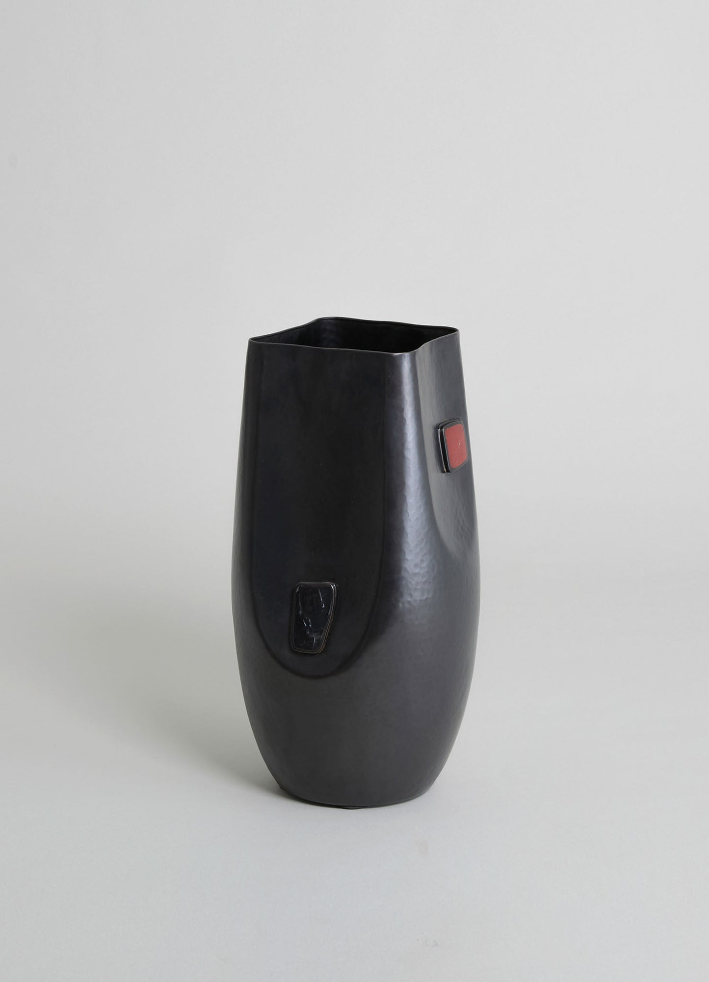 Handcrafted black ceramic vase with a hammered texture and rectangular color accents in red and black, featuring an organic, asymmetrical shape.