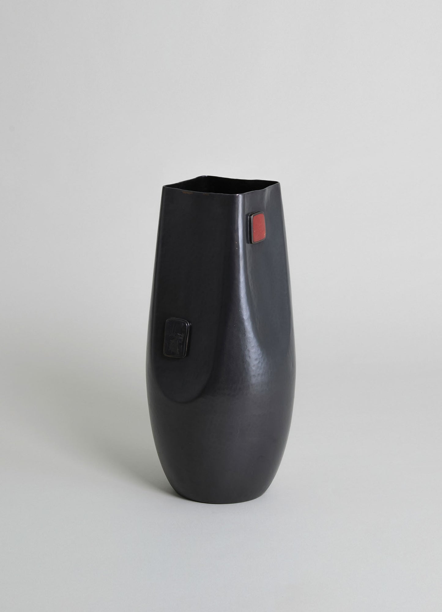 Black ceramic vase with a matte, textured surface and rectangular accent details in red and black, featuring a tapered cylindrical shape with a square opening.
