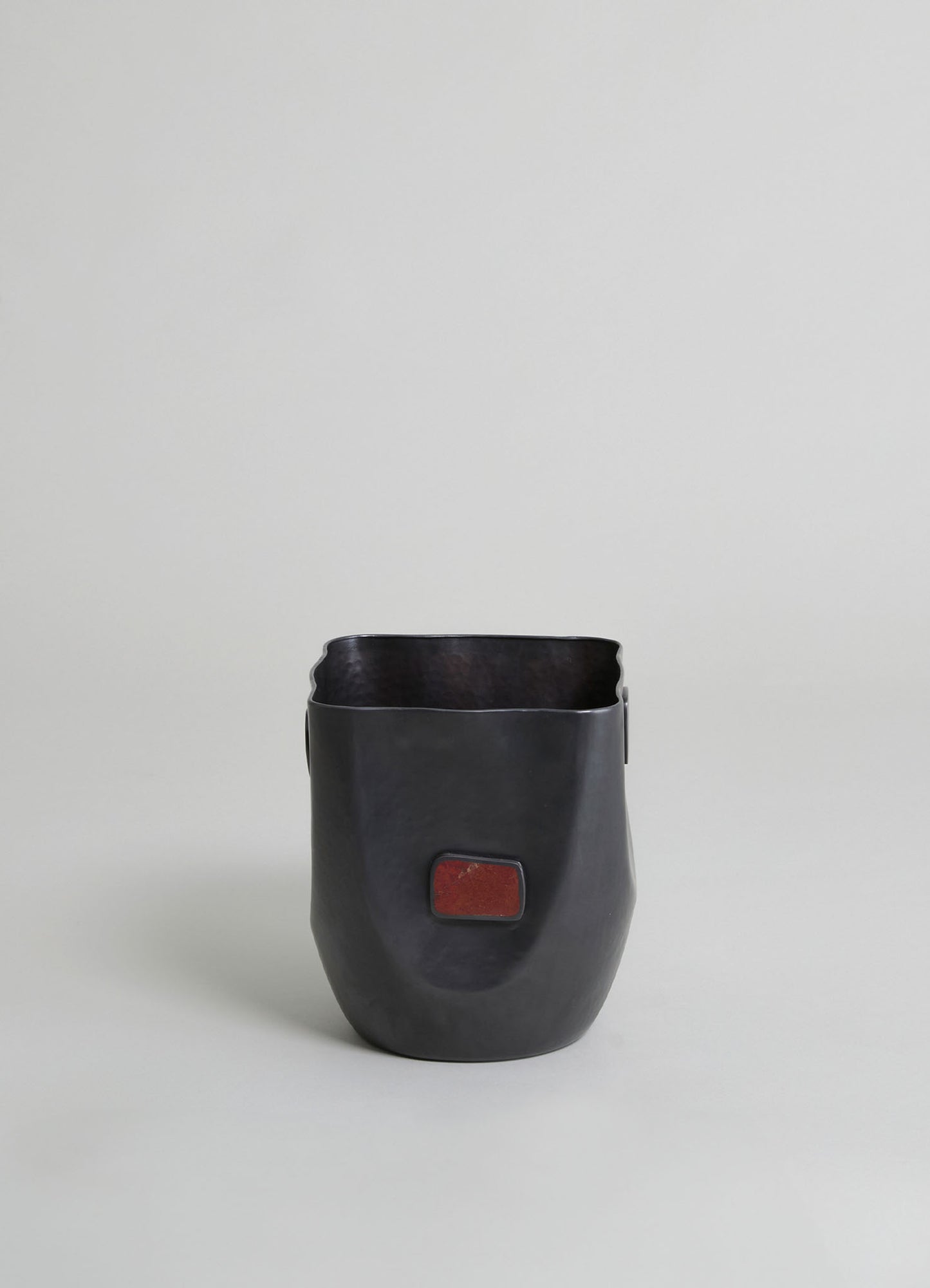 Black ceramic or clay planter with a matte finish and a rectangular red-brown accent detail on the front, featuring a rounded, slightly tapered shape.