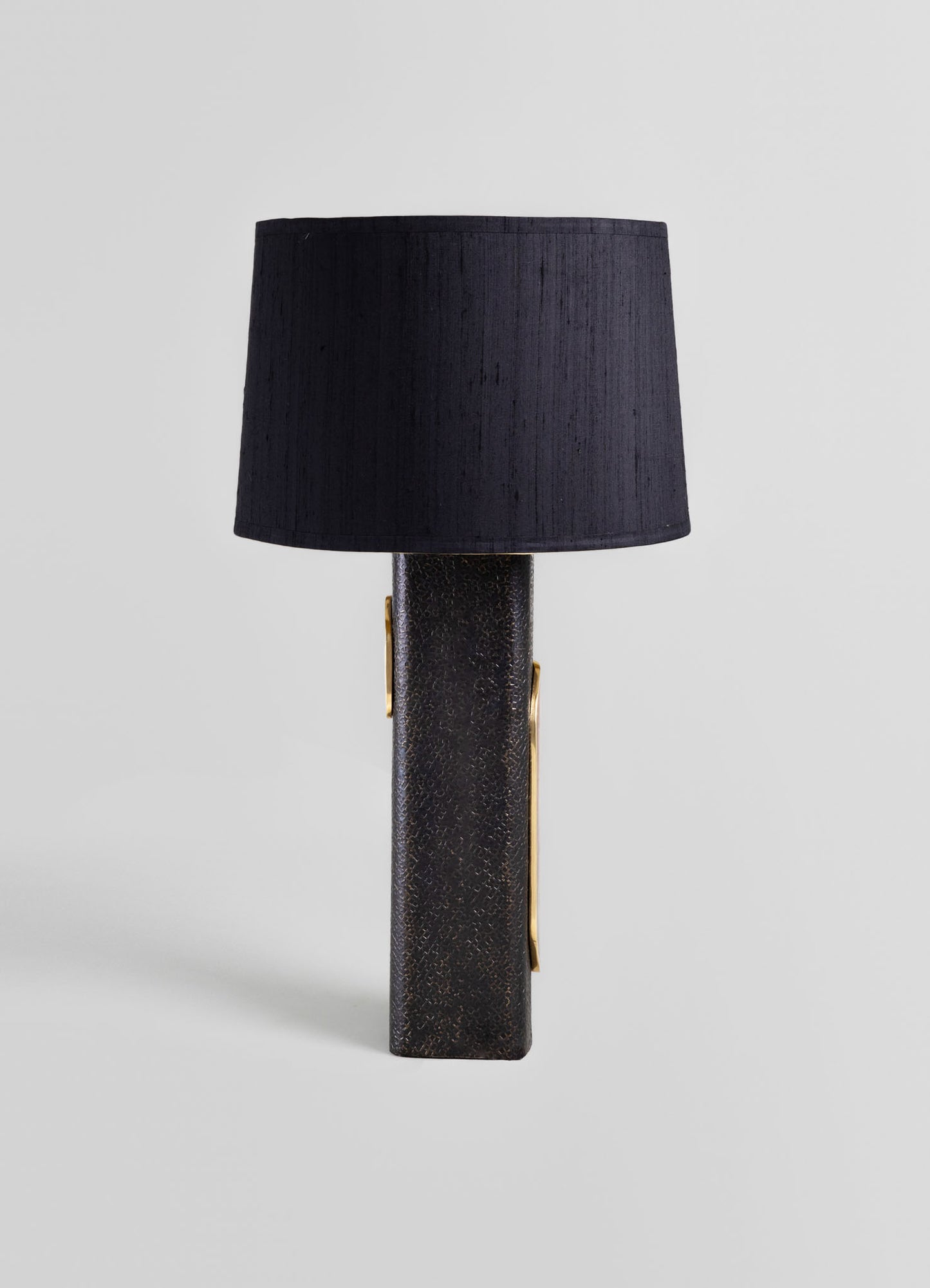 Black table lamp with a textured, cylindrical base featuring gold accents and a large black fabric lampshade, in a contemporary style with luxurious and modern design elements.