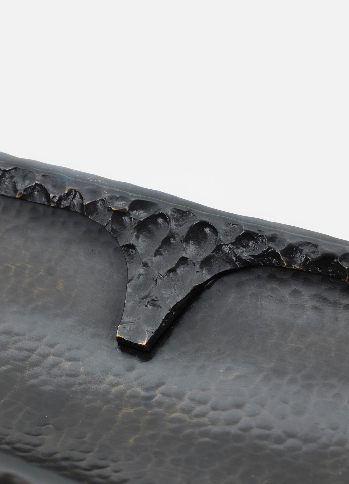Close-up of a black ceramic tray with a textured, hammered surface and a slightly raised edge. The tray has a matte finish and a simple, rustic style.