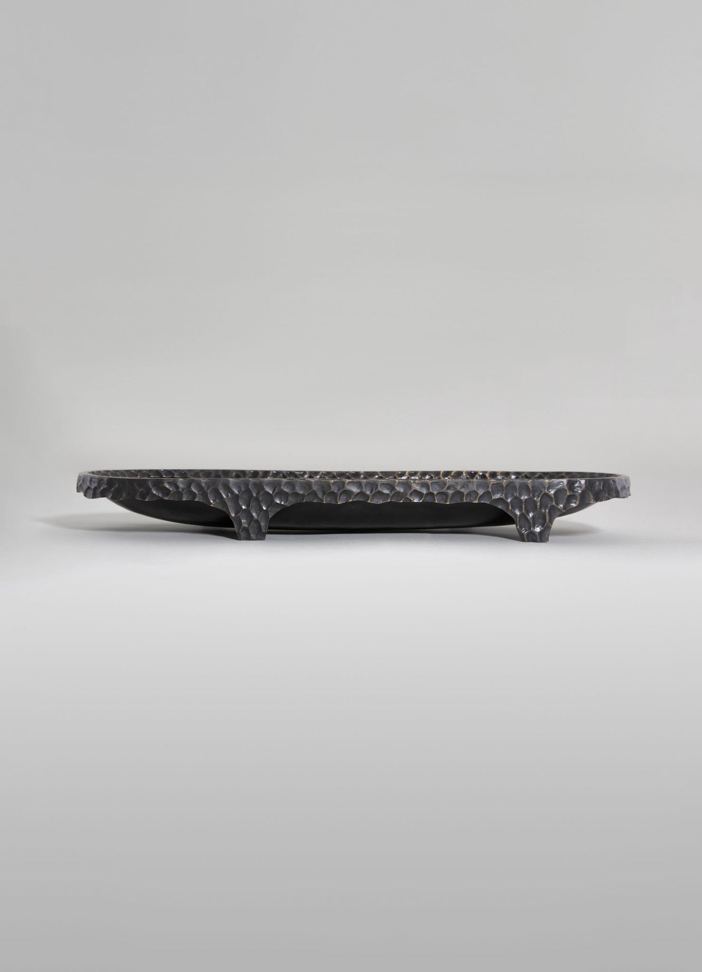A black, hammered metal tray with textured edges on curved legs, featuring a contemporary design.
