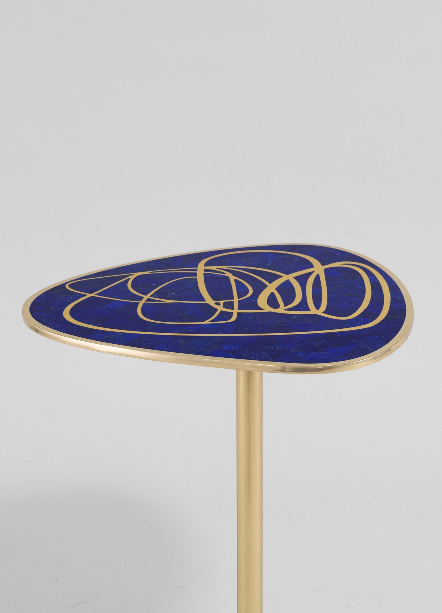 A round side table with a blue marble top featuring gold abstract line motifs and a gold metal edge, supported by a slim gold metal pedestal base.