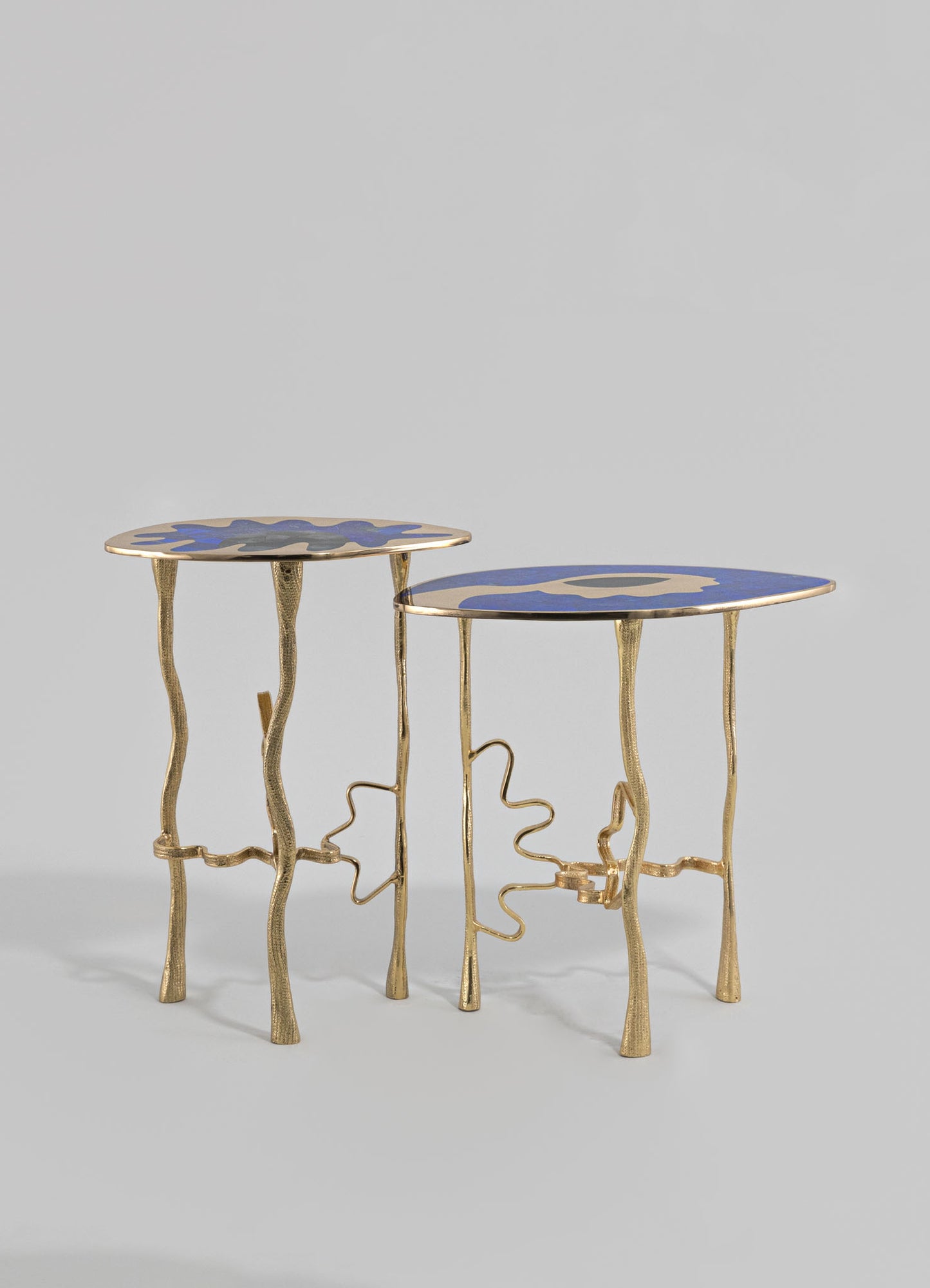 Pair of side tables with irregular, wavy metal frames in gold finish and abstract-patterned tabletops in blue and gray tones. The tables feature sculptural, artistic designs with organic-shaped legs, embodying contemporary and eclectic style.