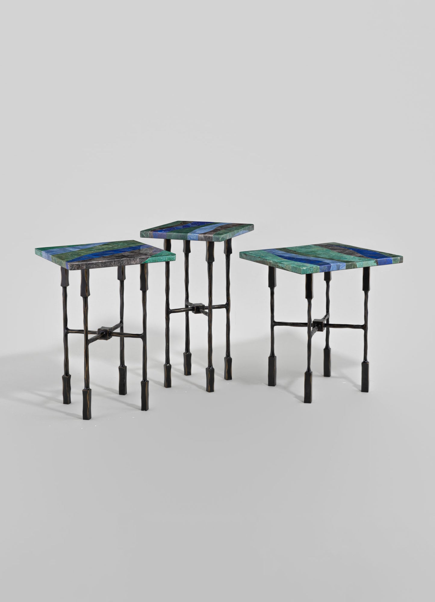 Set of three nesting tables with rectangular tops made of multicolored mosaic stone in shades of blue, green, and gray, supported by black wrought iron legs with a twisted design.