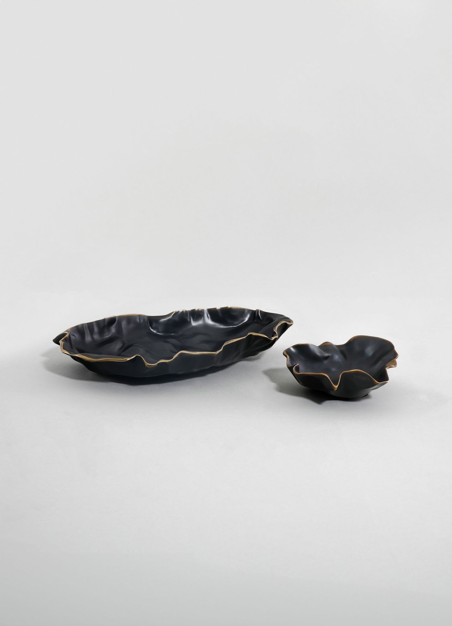 Black ceramic bowls with wavy, irregular edges and gold trim, featuring a matte finish, displayed on a plain light background.