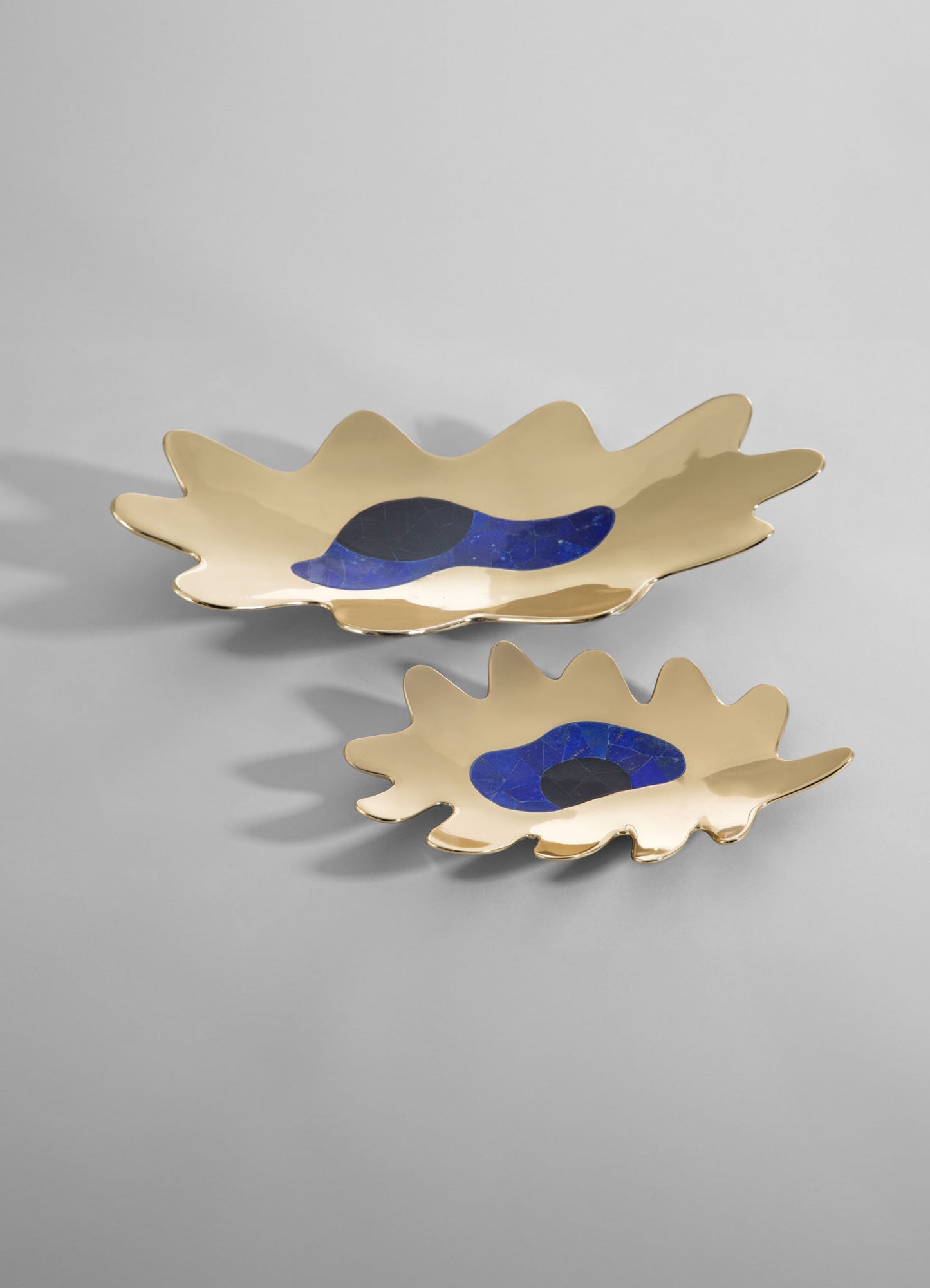 Ceramic serving dishes with gold-toned, irregularly shaped rims and blue and black abstract motifs in the center, set against a neutral background.