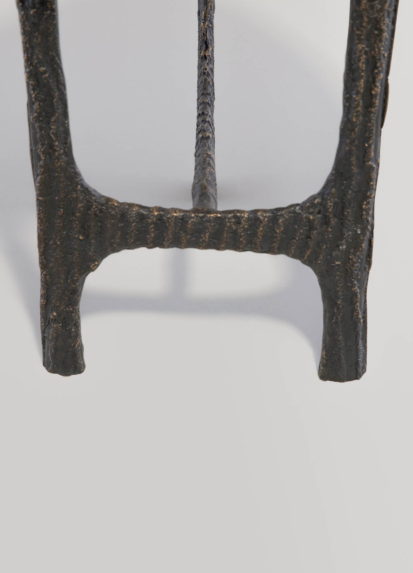 A close-up view of a textured iron or metal table leg with a rustic, blackened finish and rough, uneven surface details.