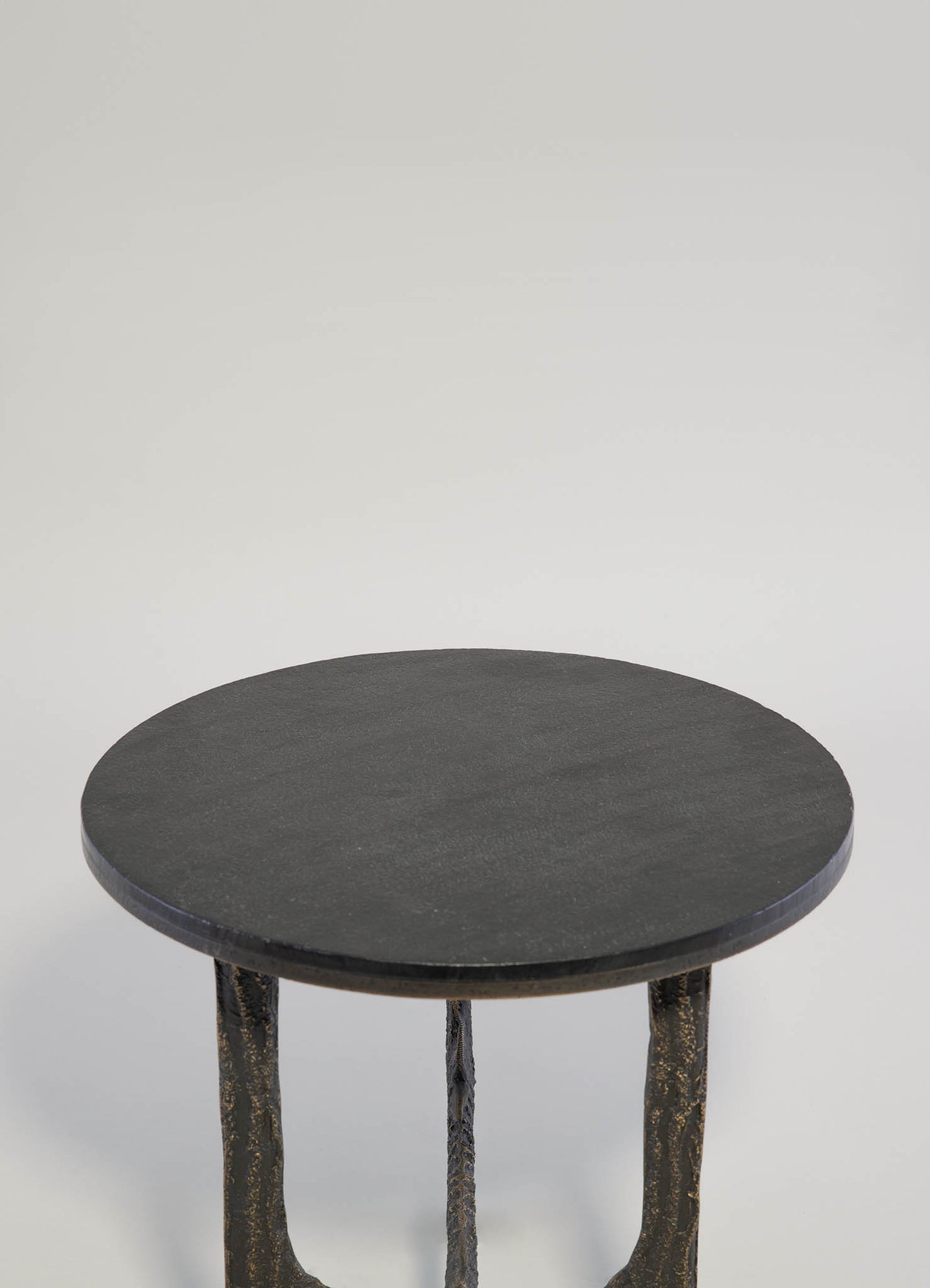 Black round side table with a textured surface and sculptural, irregular metal legs in a dark, distressed finish, showcasing a contemporary rustic style.