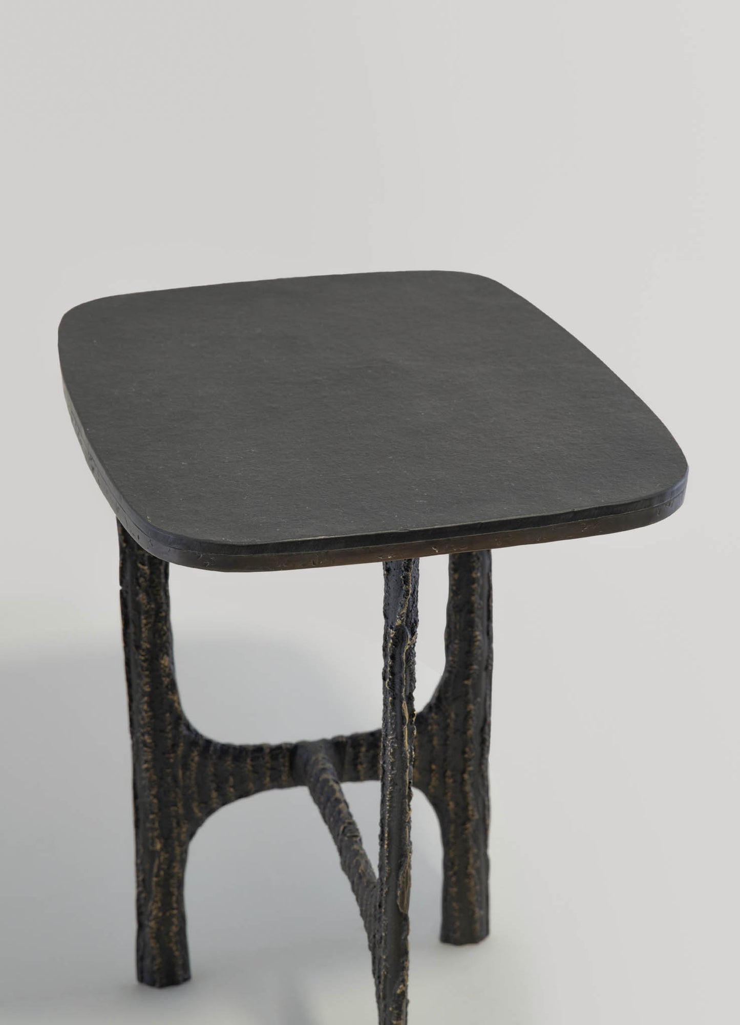 A small side table with a dark, matte stone top surface and a textured black metal base with a rustic, handcrafted appearance.