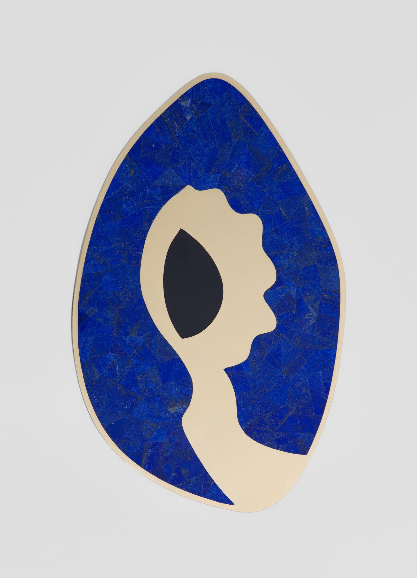 A decorative wall mirror featuring an abstract female face silhouette with a black eye patch, set against a bright blue mosaic background. The frame has an irregular oval shape, contributing to a contemporary and artistic style.