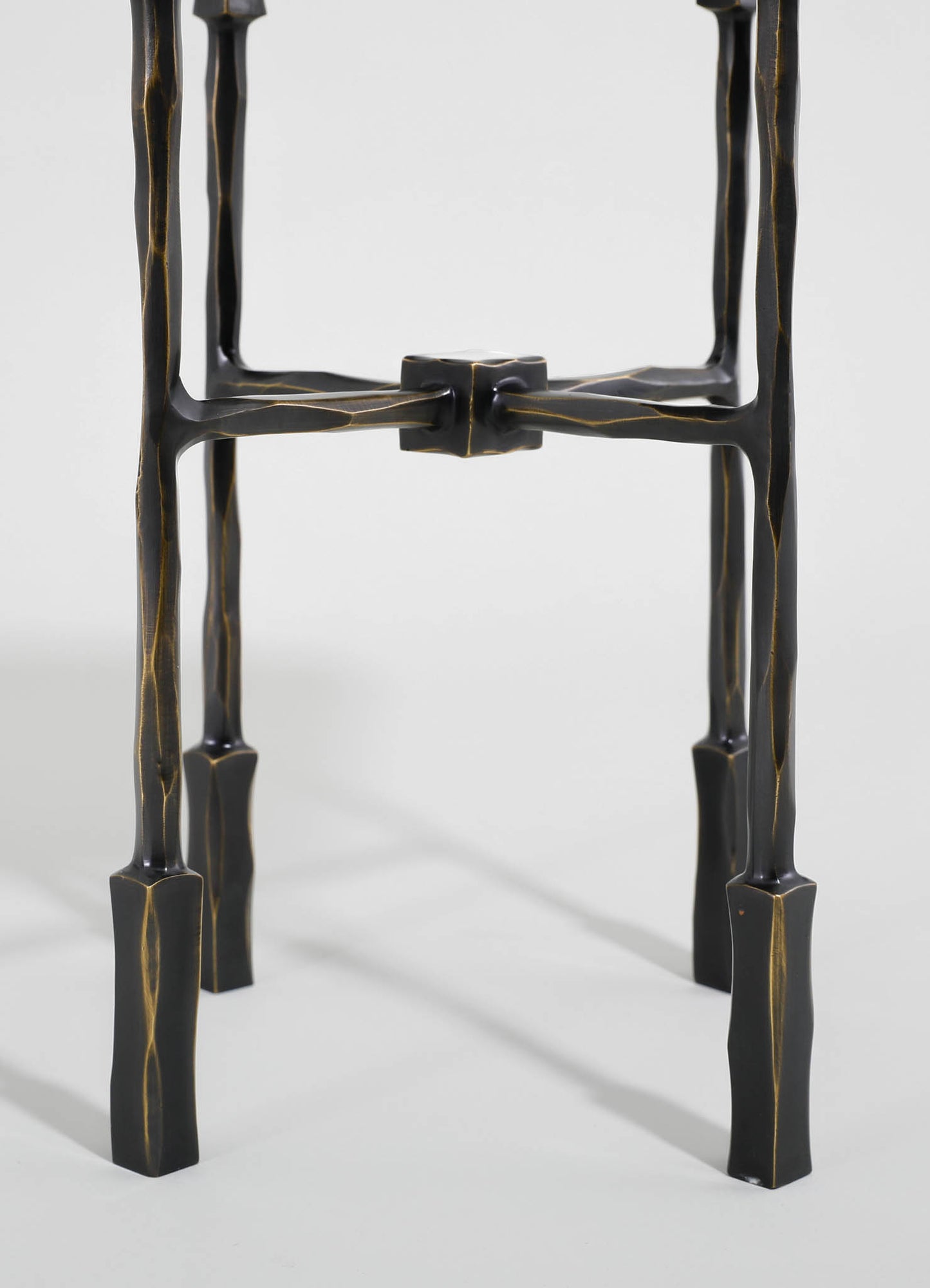 A black lacquered metal plant stand with a sculptural, irregular shape and gold-toned accents, featuring three legs connected by a rectangular central joint.