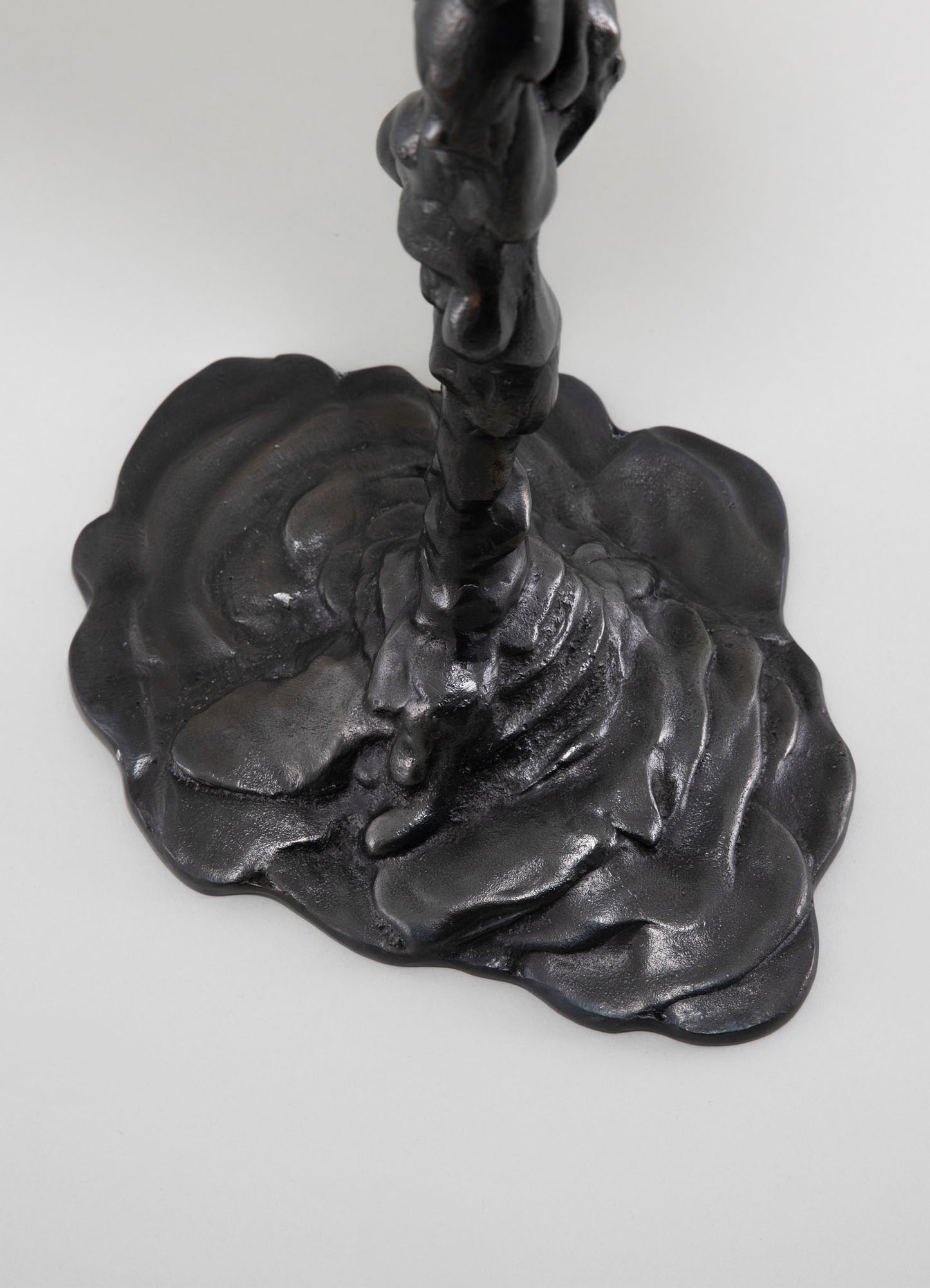Black cast iron sculpture with a textured, organic base and a tall, abstract form on top, featuring smooth, polished surfaces. The sculpture has a rustic, artistic style with a bold, monochromatic finish.