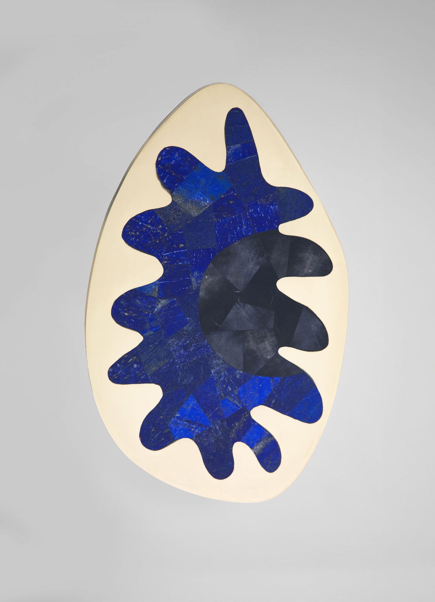 A ceramic art piece with an abstract organic shape featuring a bold blue floral motif on a cream background, with a black circular center. The design has a contemporary style with textured, painterly patterns.