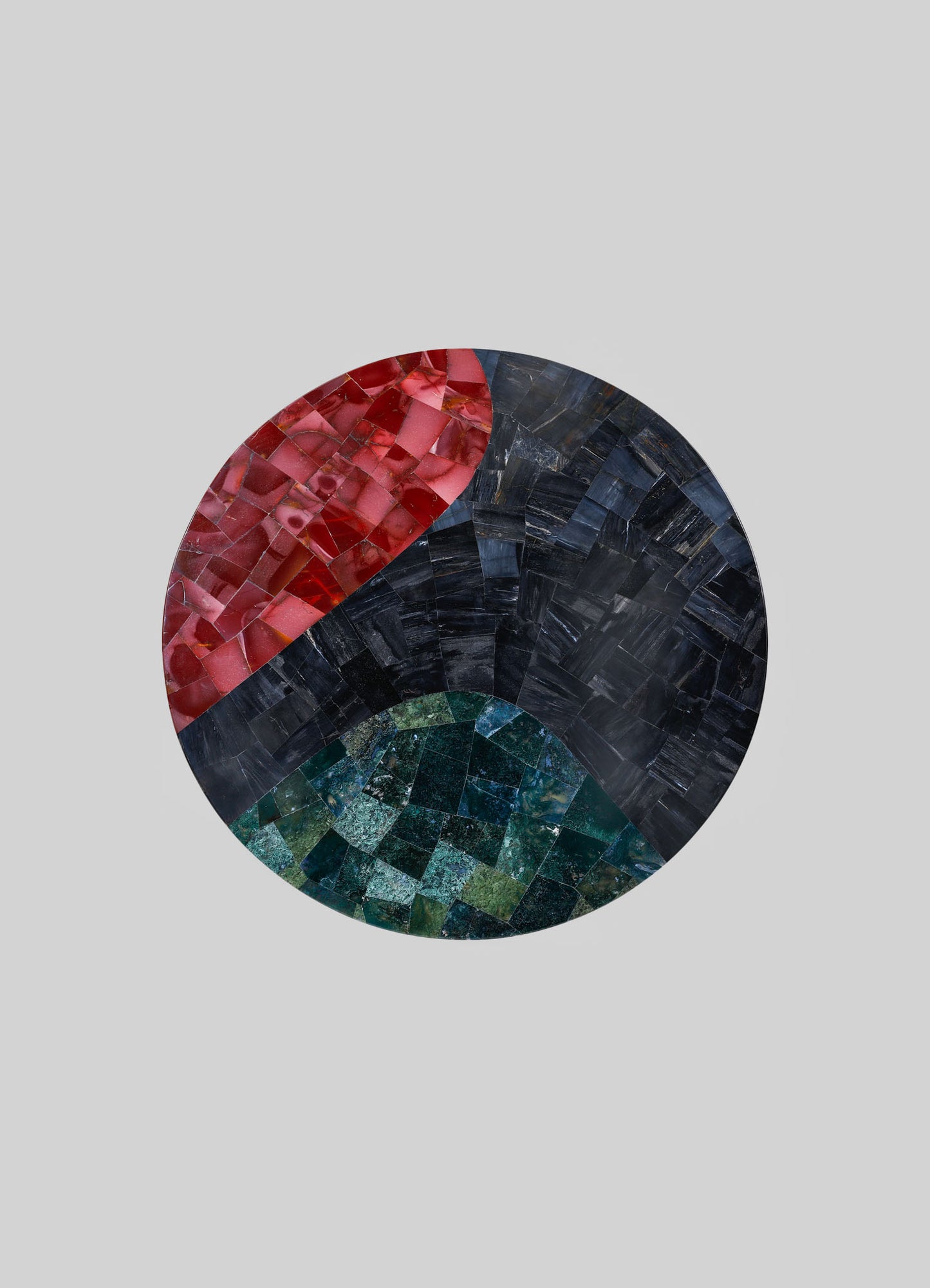 A circular mosaic art piece composed of small, glossy tiles in red, black, and green hues, arranged in abstract geometric patterns. The tiles have a mix of matte and reflective finishes, creating a textured and vibrant surface.
