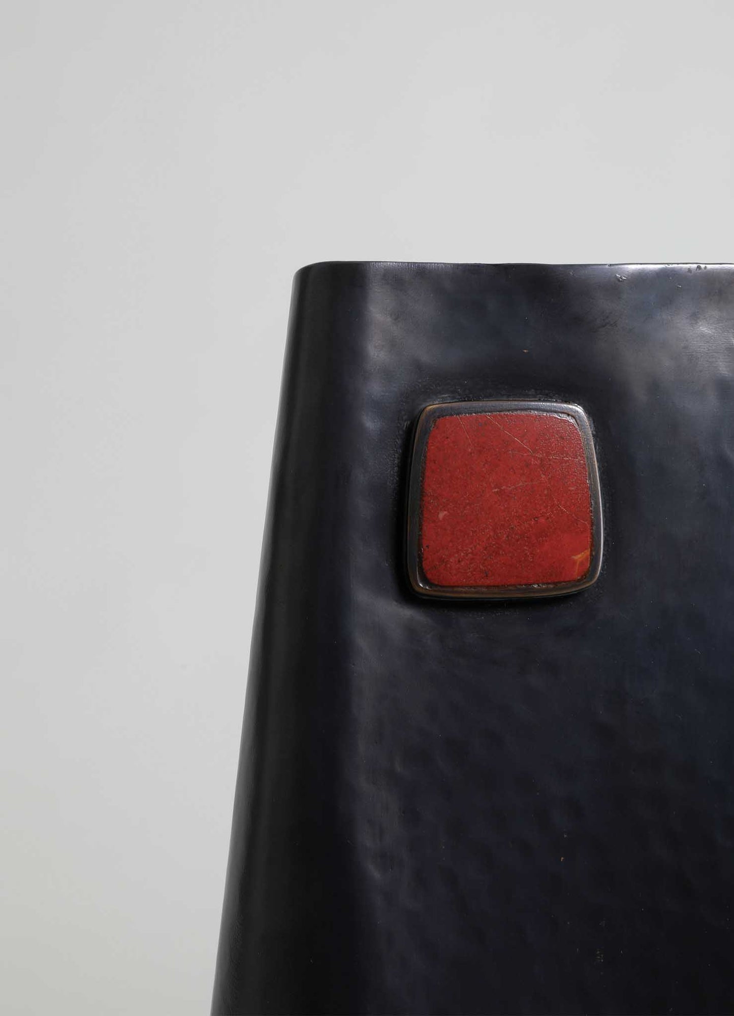 A black ceramic vase with a matte finish featuring a square red accent on its surface, with a smooth, curved shape and minimalist design.
