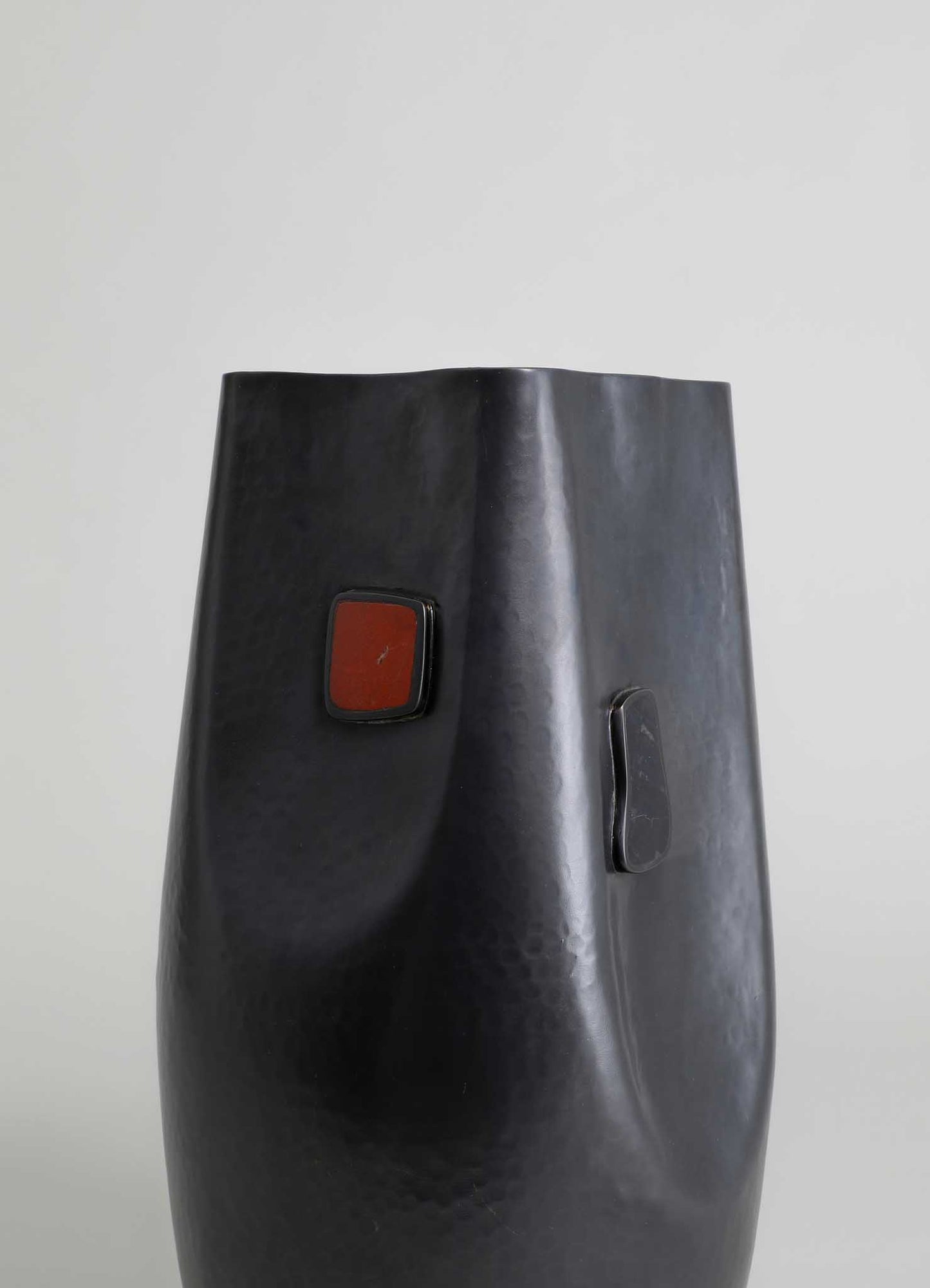 Metal vase with a hammered black finish, featuring geometric red and black accents and a sleek, modern silhouette against a plain background.
