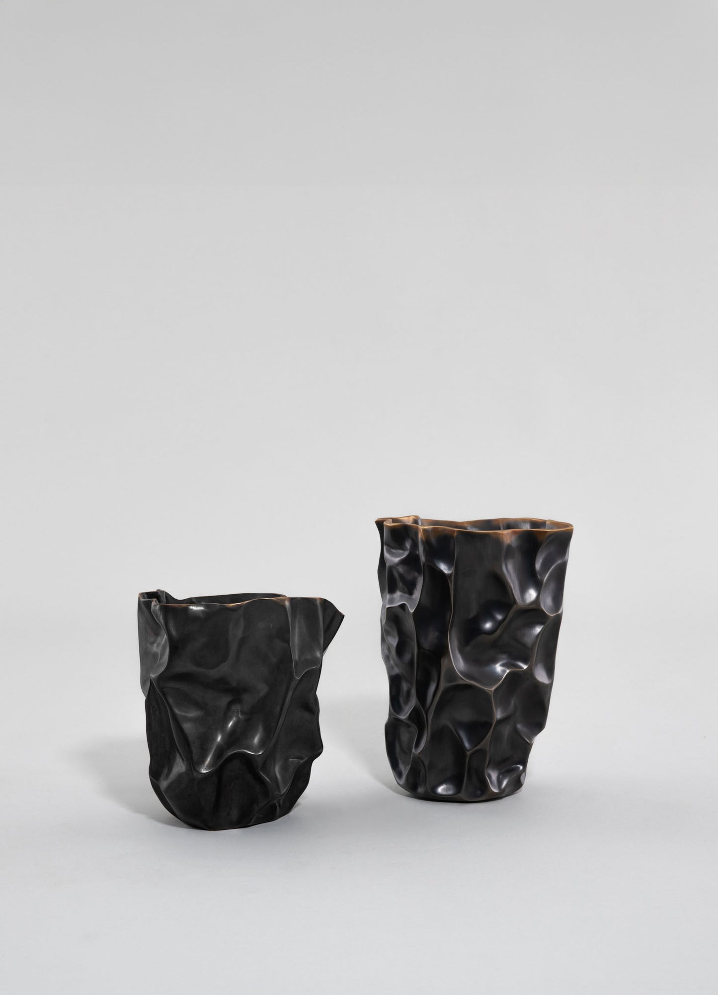 Two black ceramic vases with irregular, textured surfaces and a glossy finish, one taller than the other, positioned on a plain light gray background.