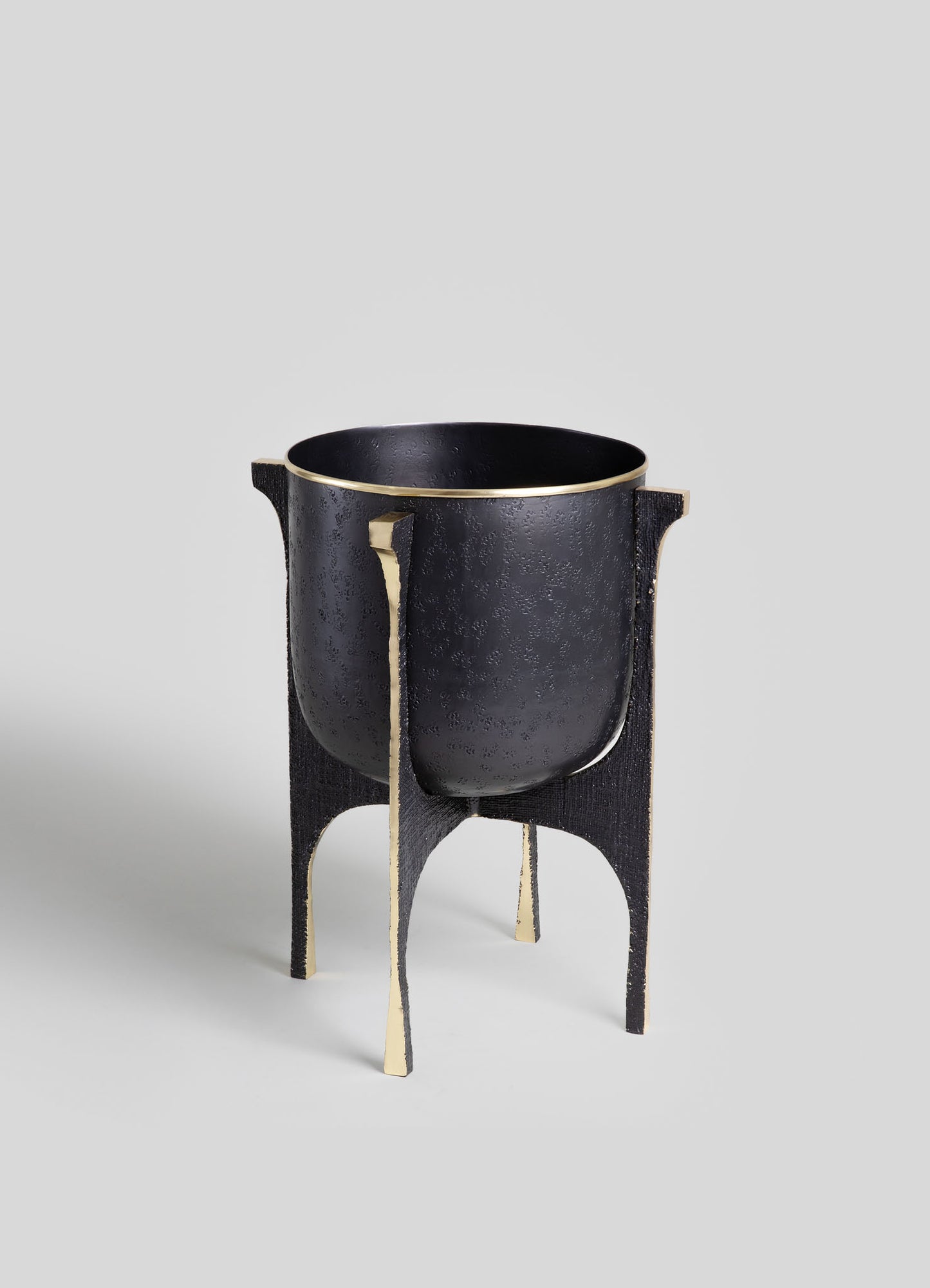 A black metal planter with a textured surface, accented with gold trim, supported by a black and gold stand with curved legs.