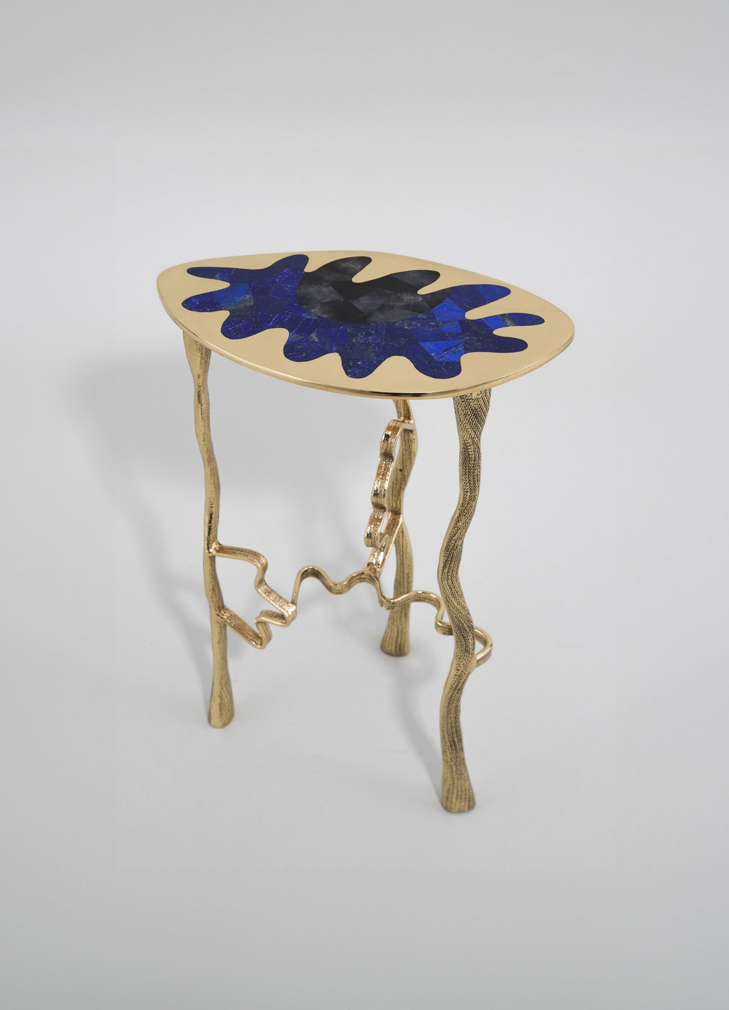 A small accent table with a round top featuring an abstract pattern in shades of blue and black, and a glossy finish. The table has a sculptural, gold-colored metal base with irregular, wavy legs.