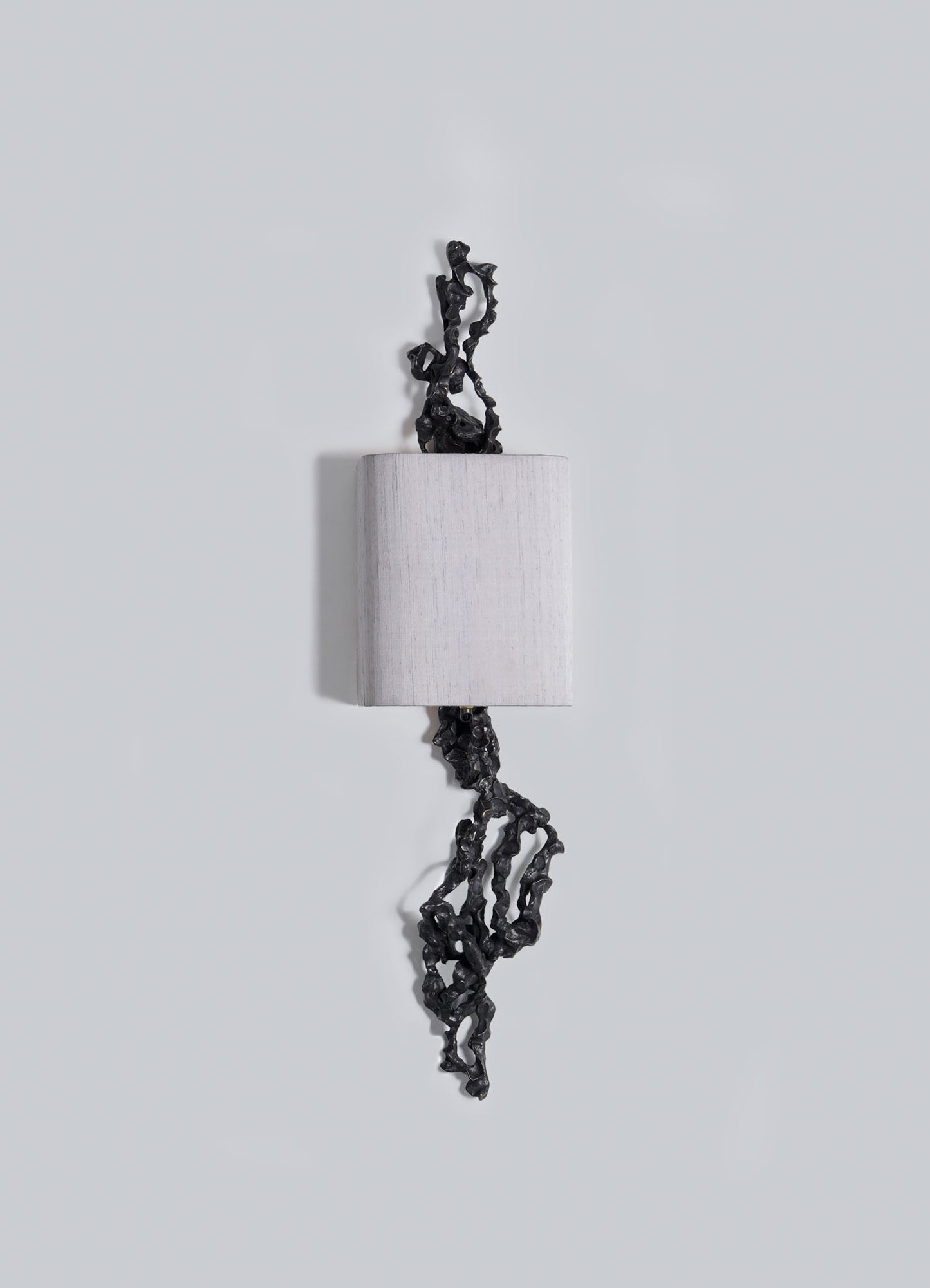 The Andaman Wall Sconce B by VIYA features a cylindrical white form on a light grey background, with irregular black accents—resembling organic shapes—extending from its top and bottom.